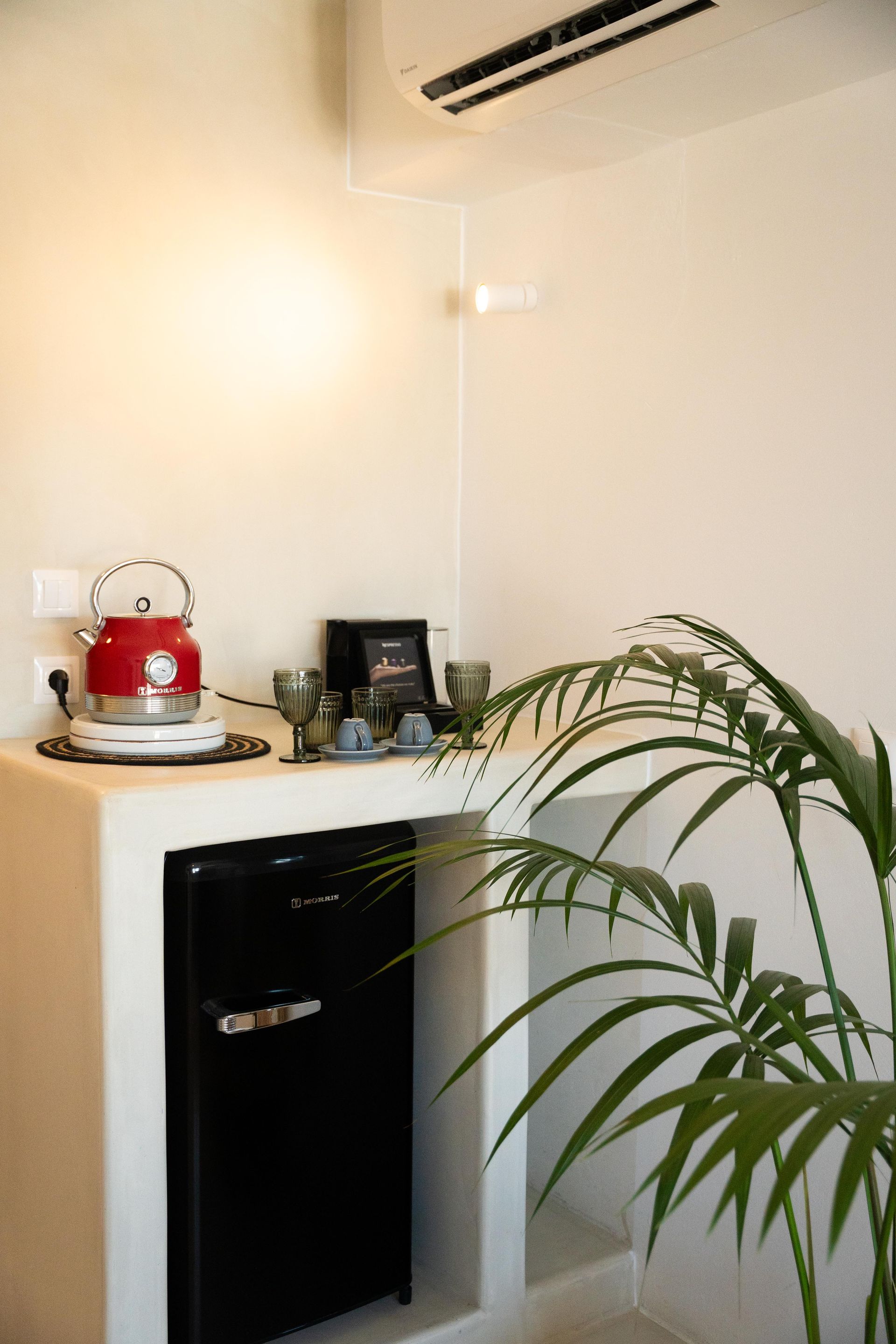 Small kitchenette with red kettle, black mini-fridge, glasses, and plant.