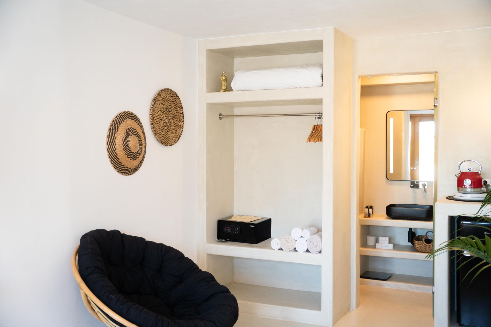 Bright white room with built-in closet, black chair, woven wall decor, and doorway to bathroom.