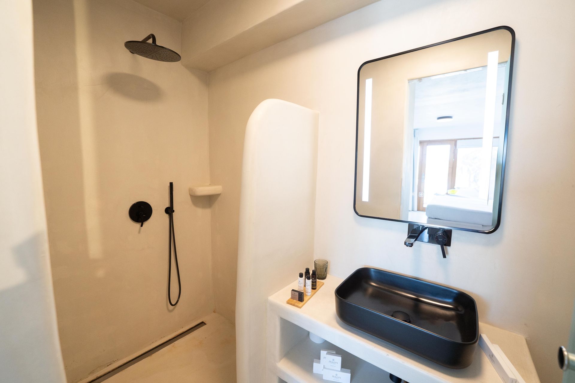 Bathroom with black fixtures, shower, rectangular sink, and large, illuminated mirror.