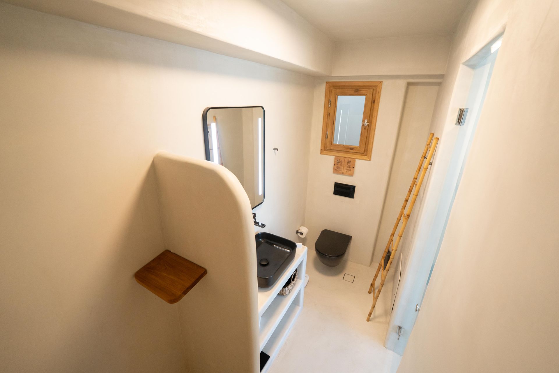 Small, white bathroom with black sink and toilet, wood accents, and a decorative ladder.