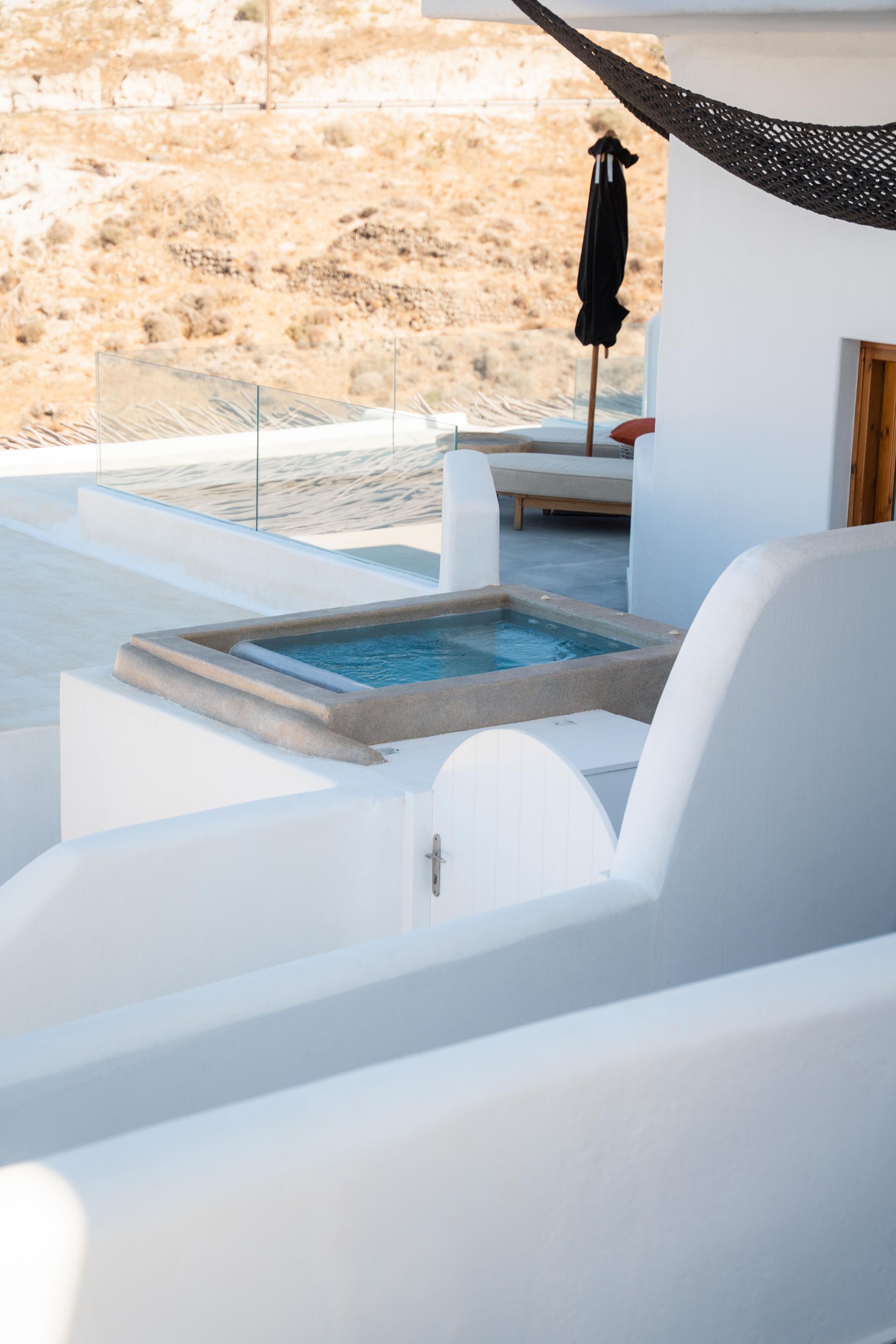 White-walled luxury outdoor space with a small pool, overlooking a dry landscape.