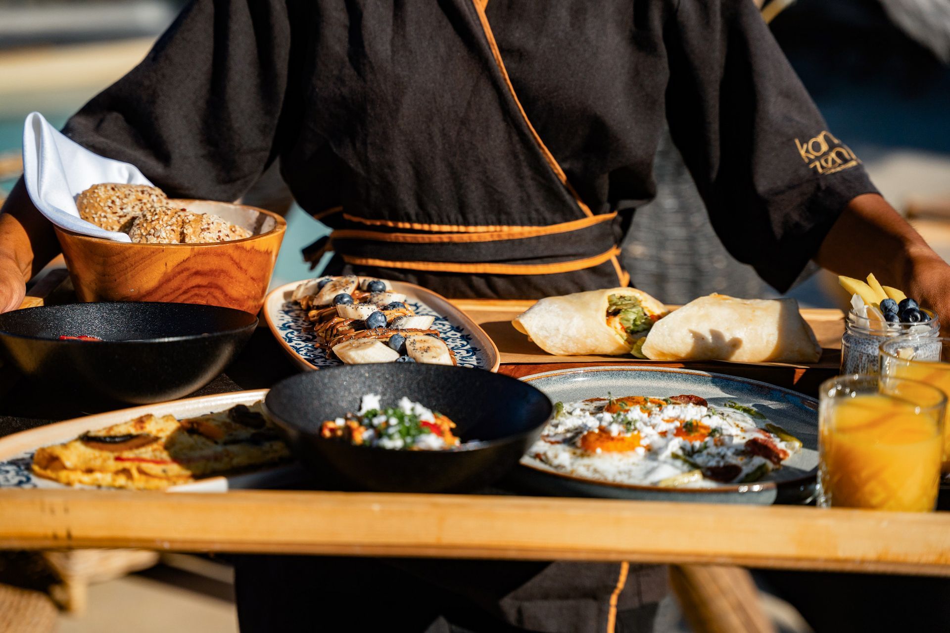 Person holding a tray of food outdoors. Includes bowls, wraps, and drinks.
