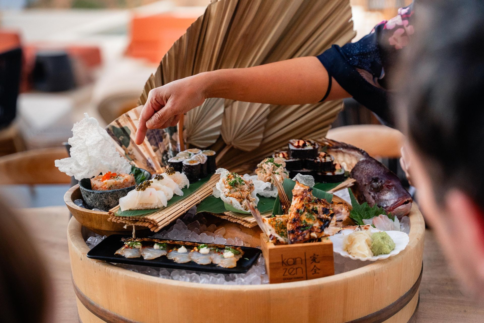 Sushi platter on ice, being served outdoors; hands reach for pieces, various rolls.