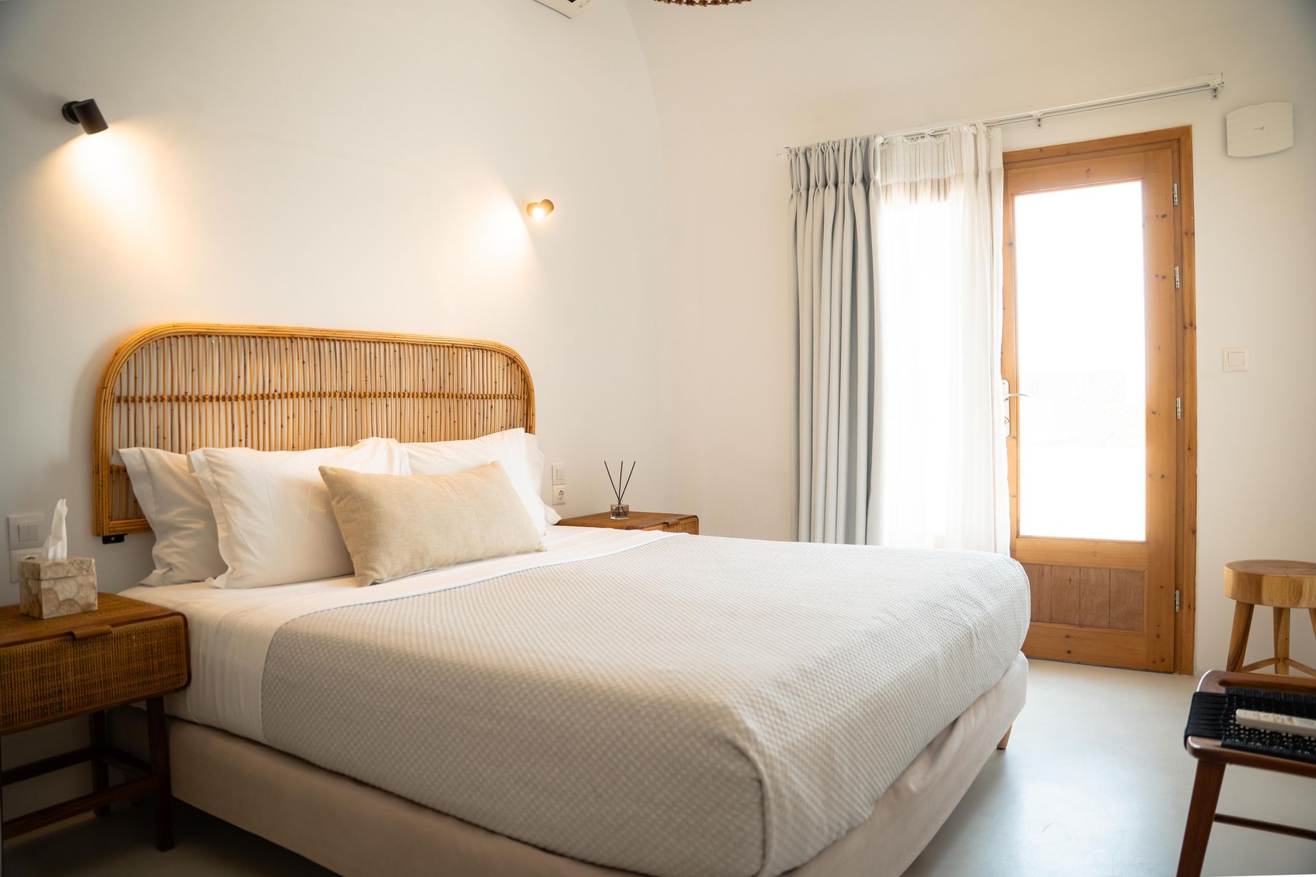 Bedroom with a rattan headboard, white bedding, wooden nightstand, and door to natural light.