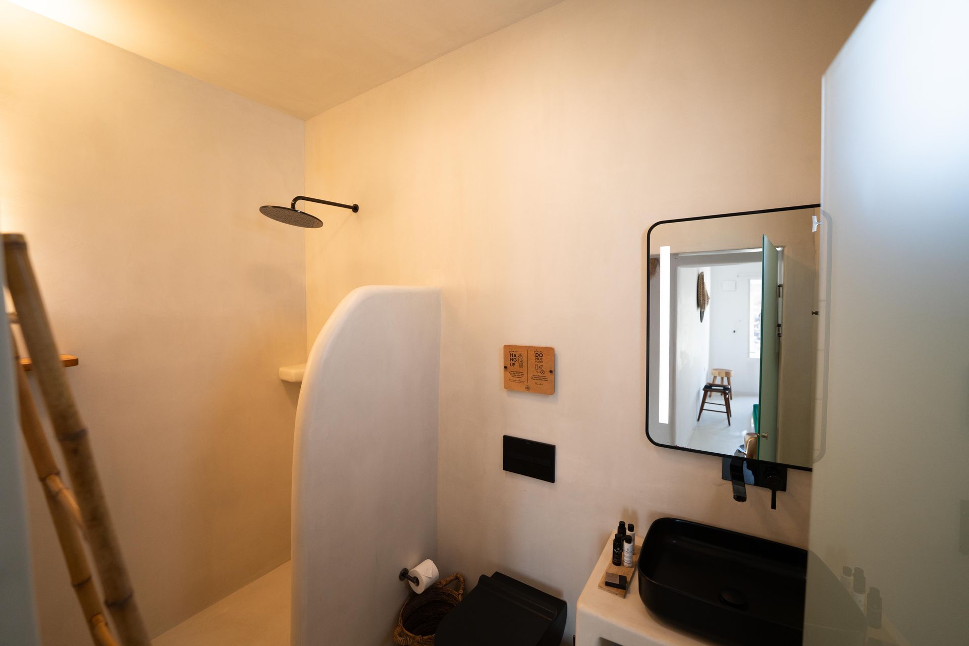 Bathroom with white walls, black sink, open shower with shower head, mirror.