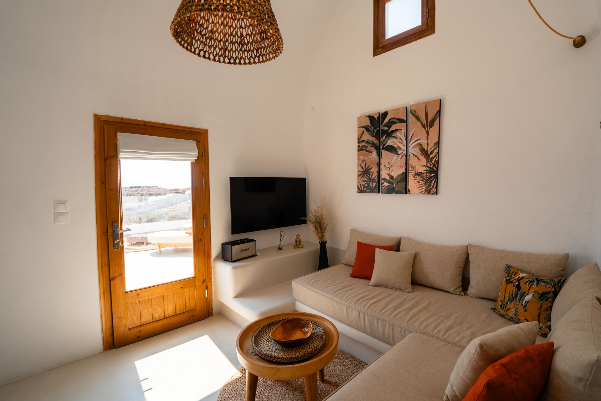 Bright living room with tan sofa, wood door, and palm tree art.