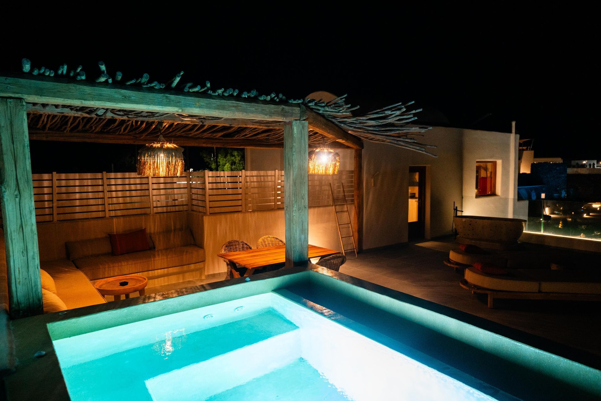 Rooftop pool with seating area under a wooden pergola, illuminated at night.