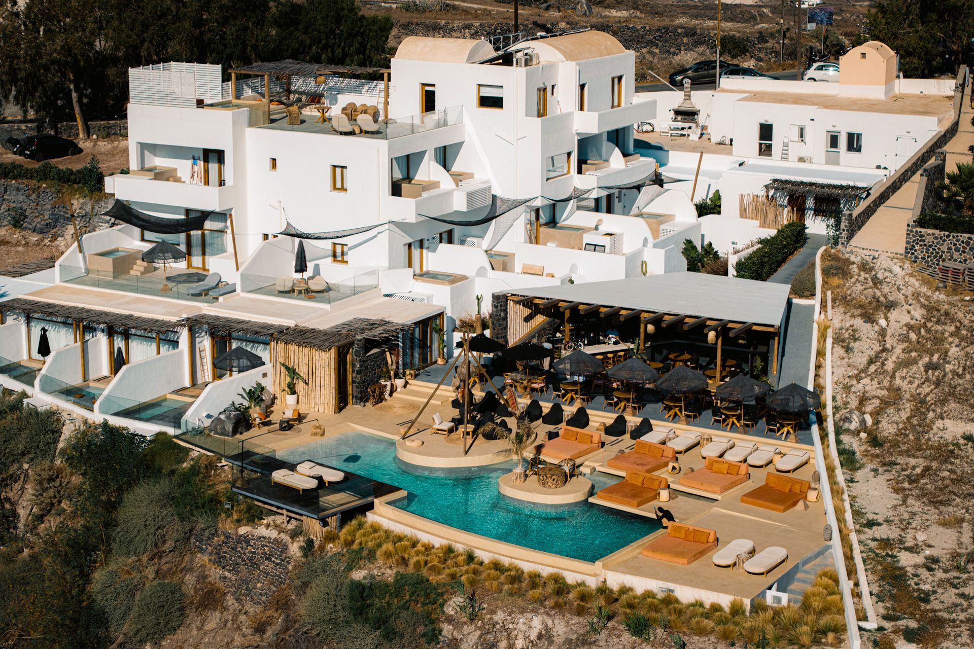 White-washed hotel with pool, loungers, and shaded dining area. Santorini, Greece.