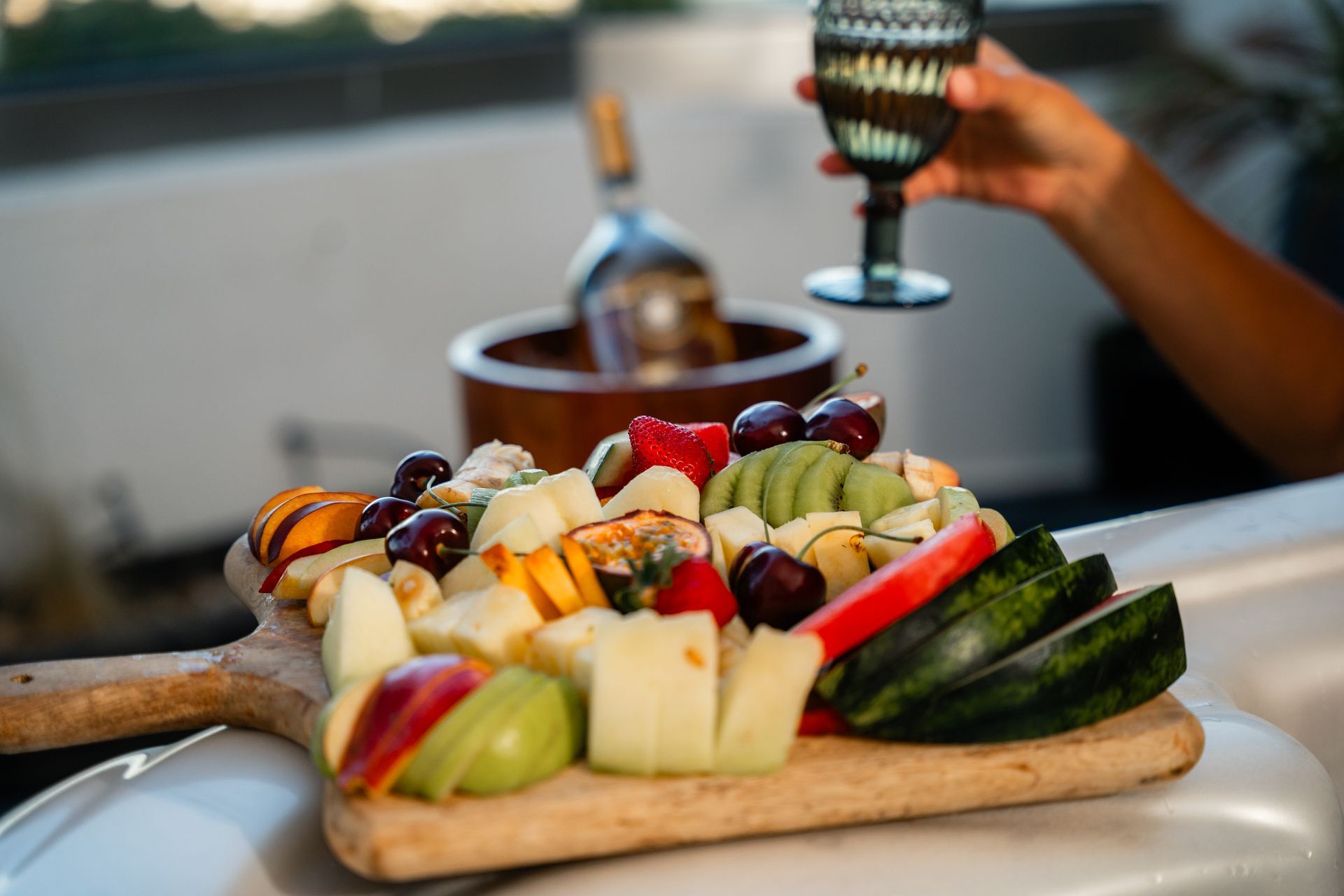 Fruit platter with wine glass; person holding glass near bottle in ice bucket.