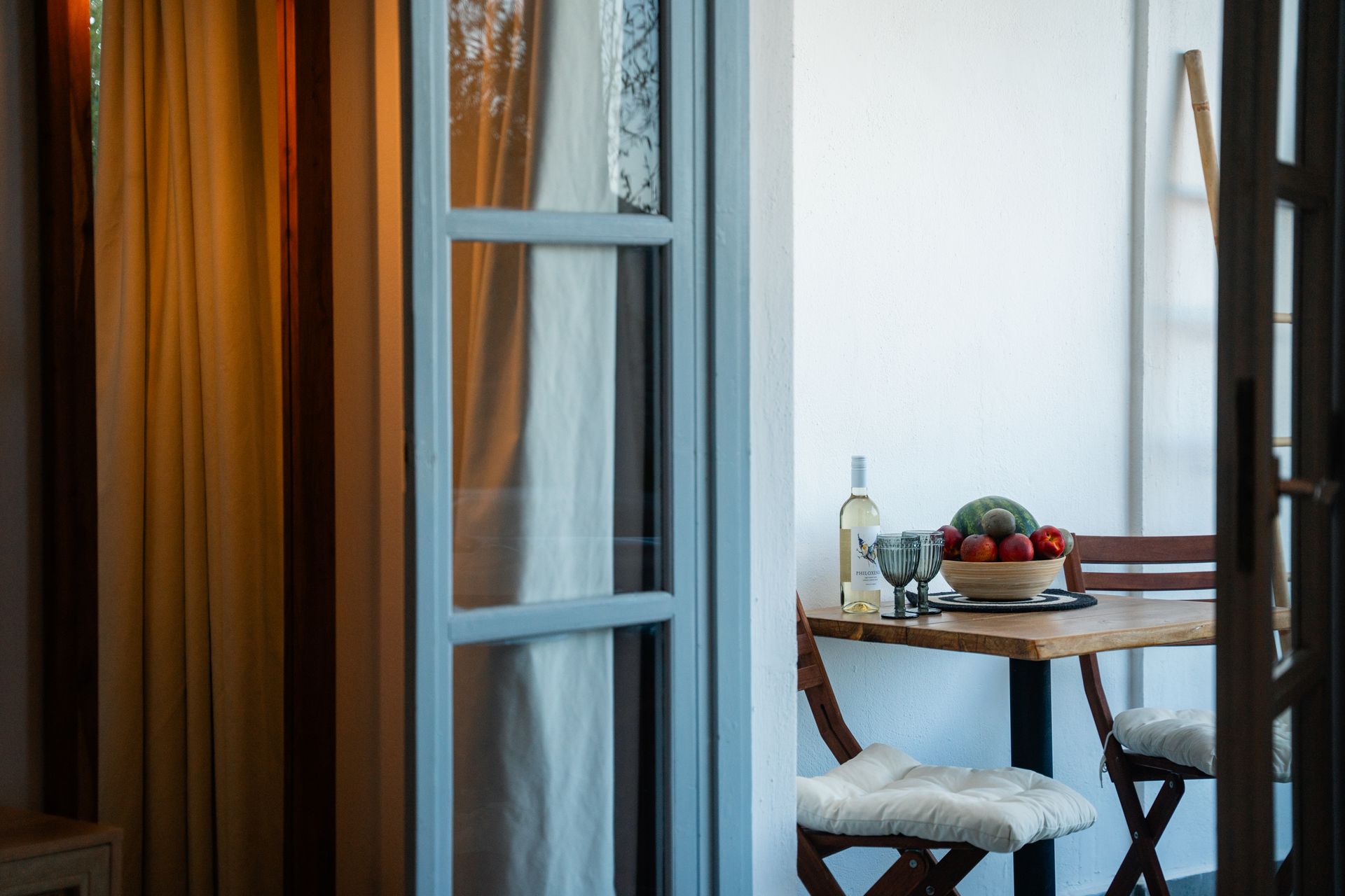 Balcony with a small table set for two, with wine, fruit, and white chairs.