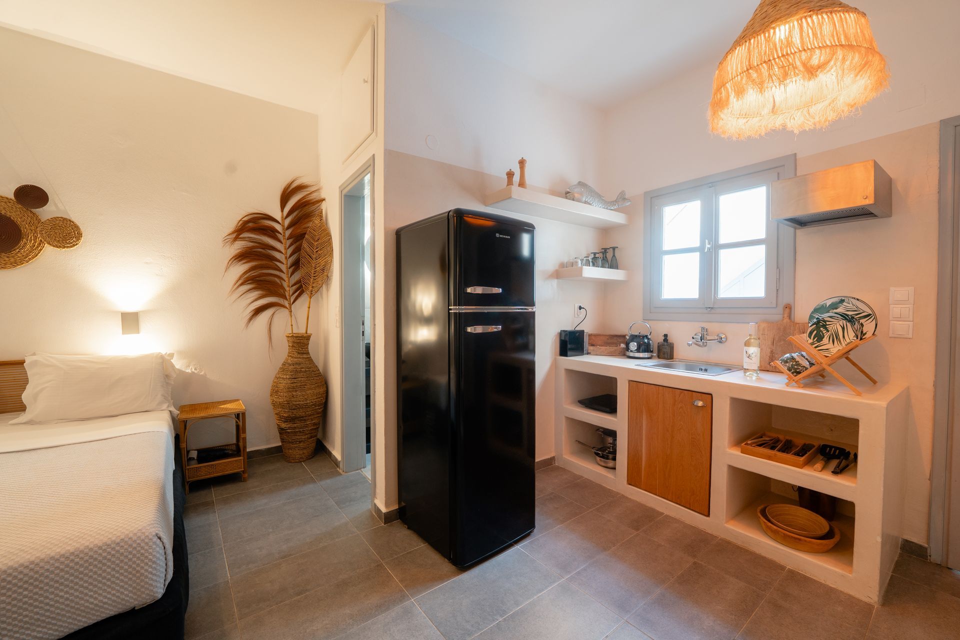Small studio apartment with a kitchen, bed, and black retro refrigerator.