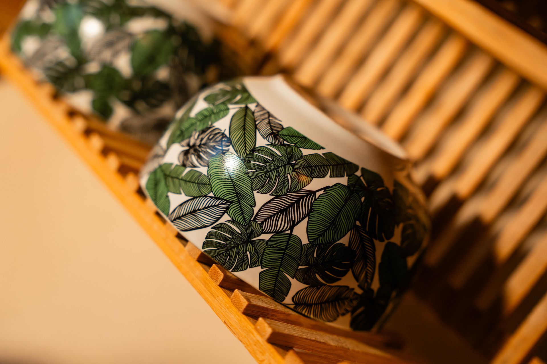 Two white bowls with green leaf patterns in a wooden drying rack.