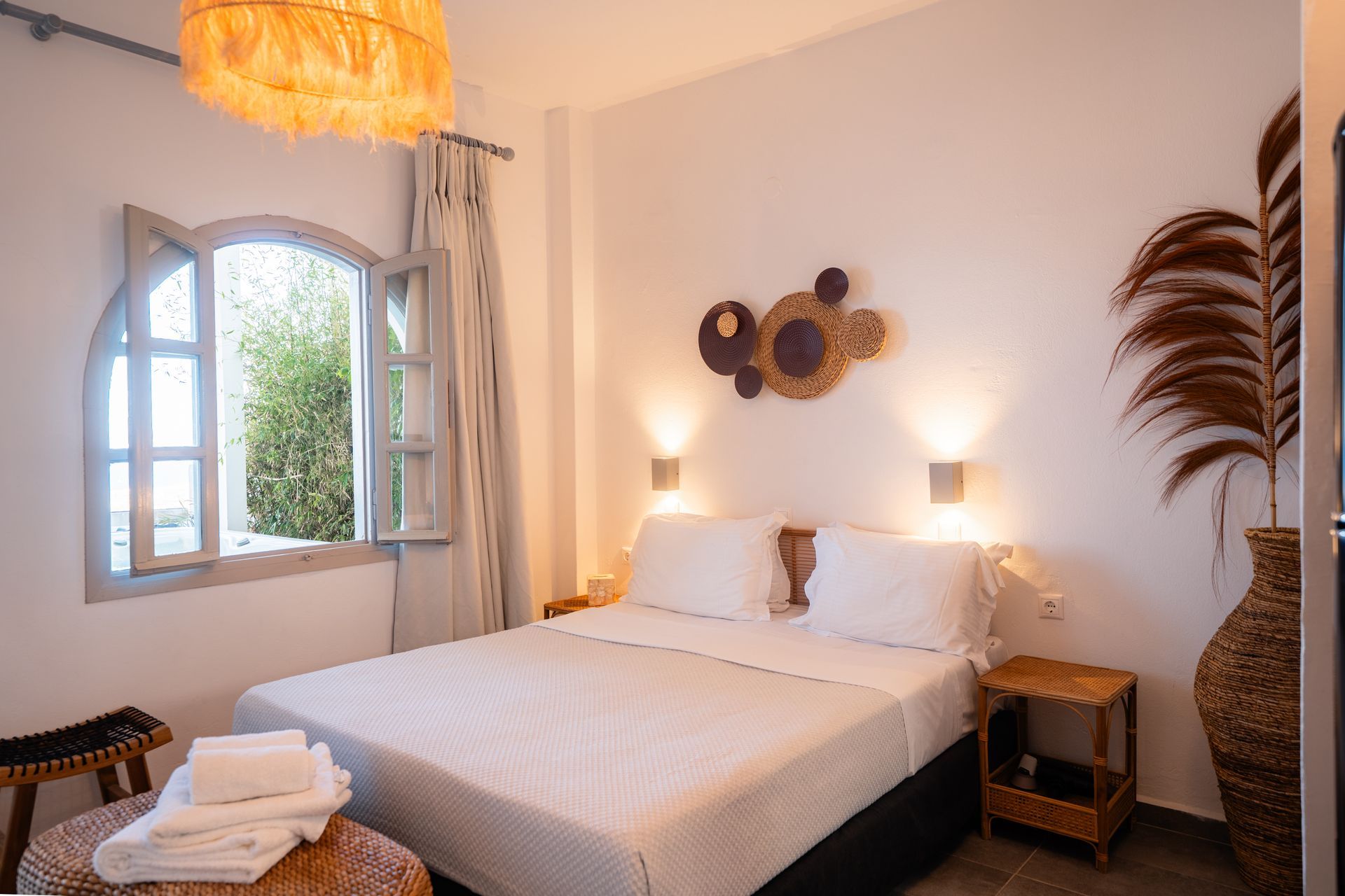 Cozy bedroom with white bedding, a decorative wall hanging, and a view through an arched window.