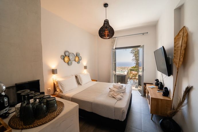 Bright bedroom with a bed, bedside lamps, wall decor, TV, and open balcony doors overlooking the sea