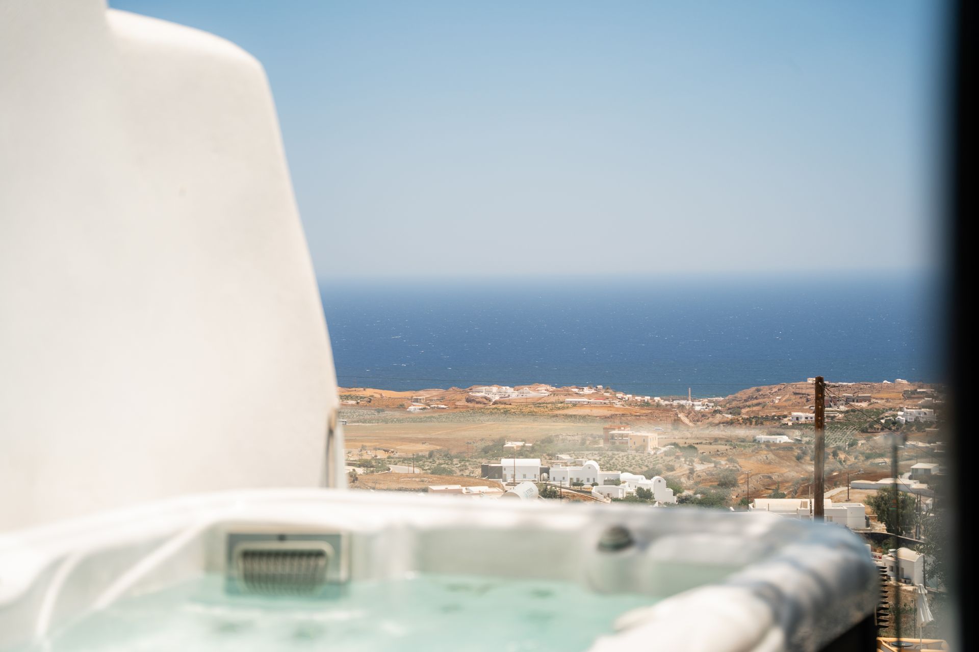 Hot tub overlooking a blue sea and buildings on a sunny day.