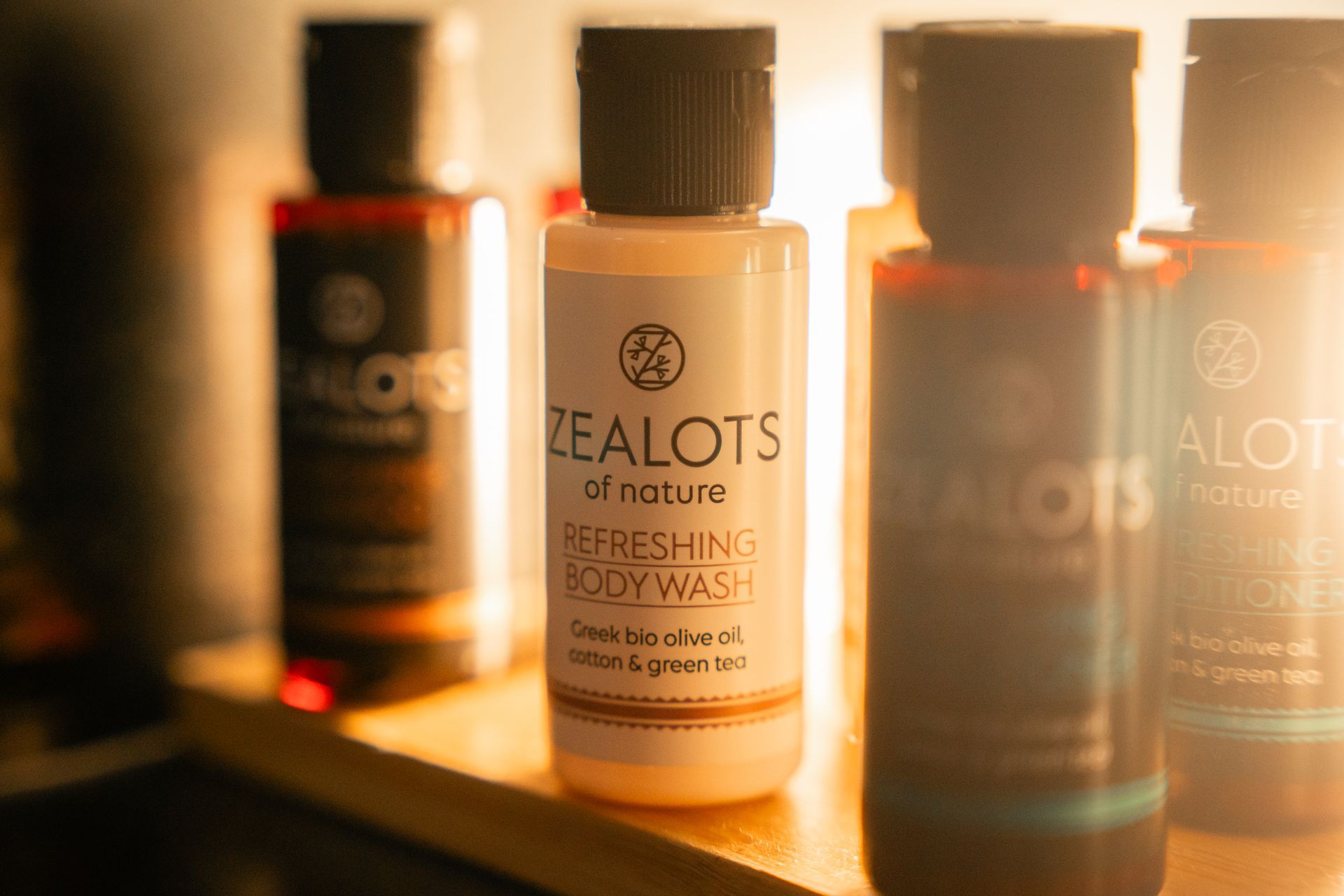 Bottles of Zealots of Nature body wash; white and brown labels, Greek olive oil, on a shelf.