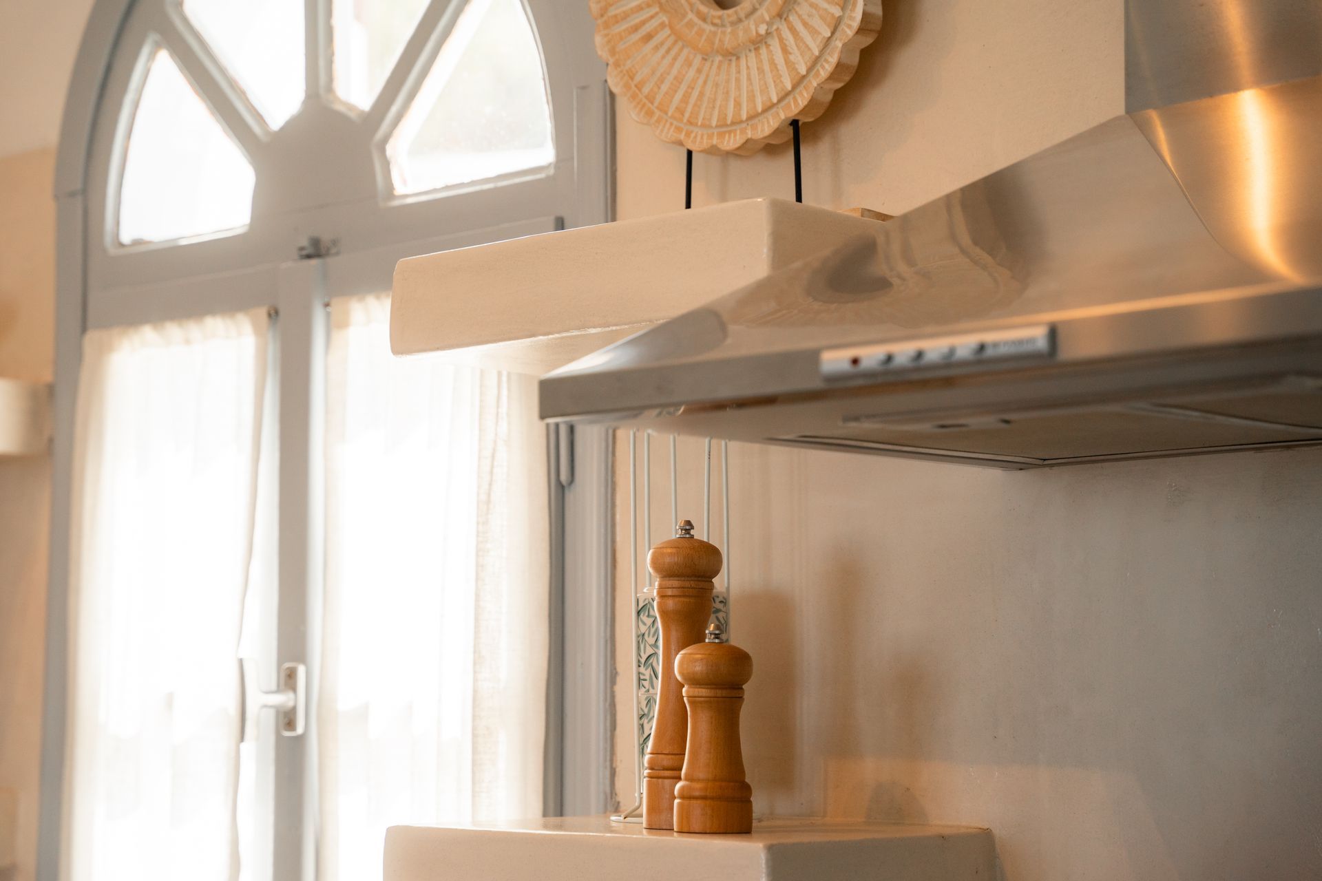Kitchen with wooden pepper grinders, stainless steel range hood, and arched window.