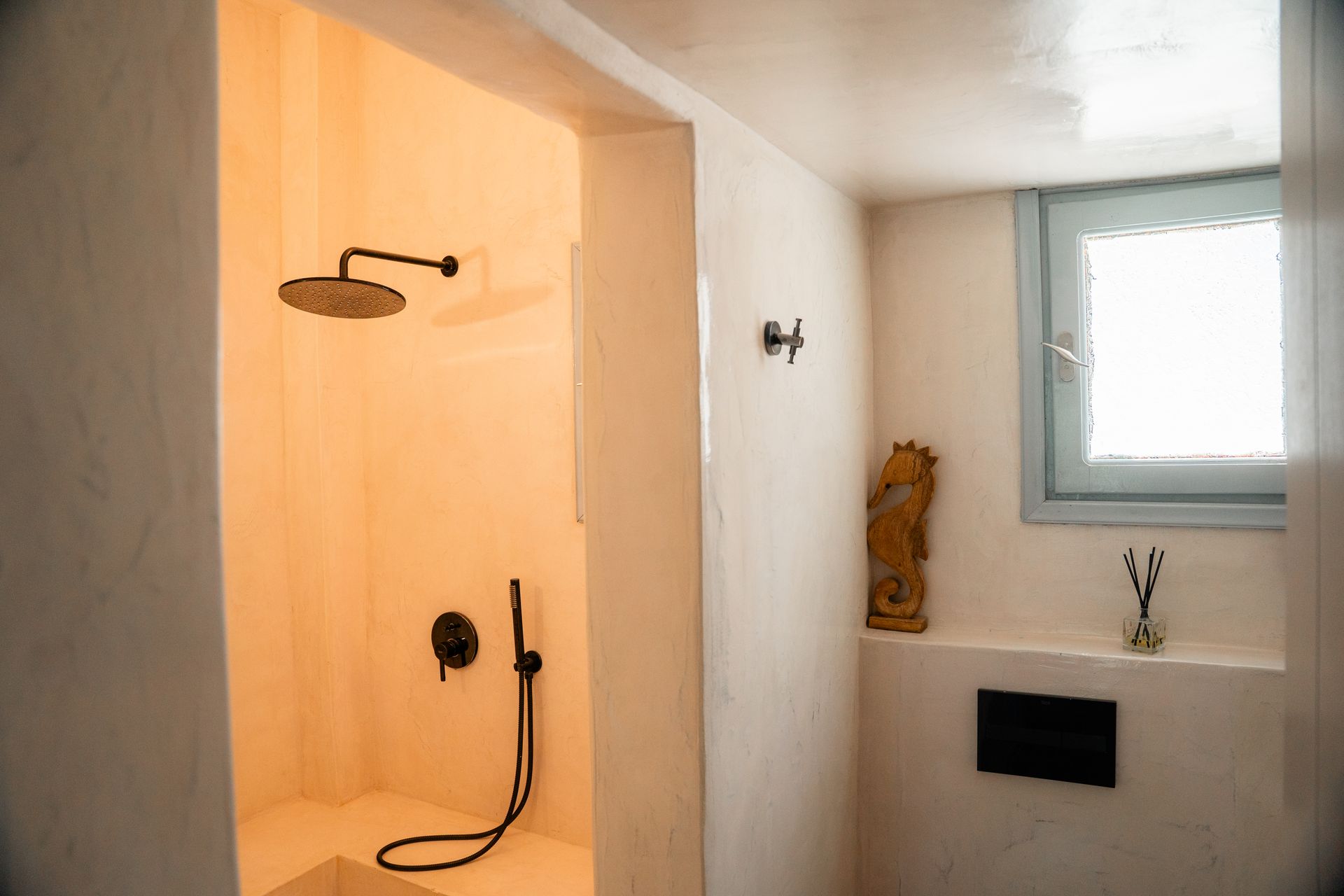 Bathroom with a walk-in shower and small window. Light walls, dark fixtures, and a small carved wooden statue.