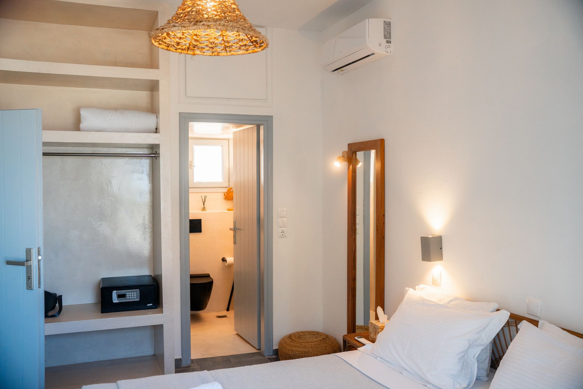 Bedroom with closet, bathroom, bed, and tall mirror; white walls and soft lighting.