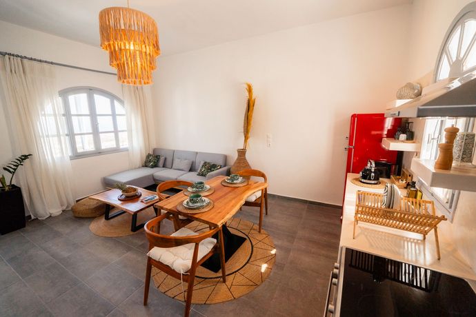 Bright living room with couch, dining table, pendant light, and kitchenette with red appliances