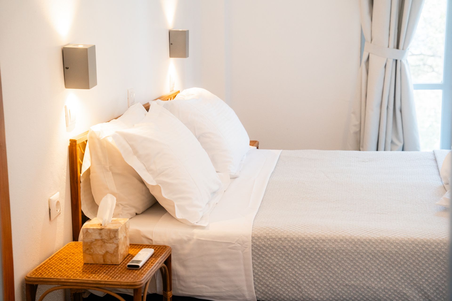 Bedroom with white bedding, bedside table, and sconce lighting.