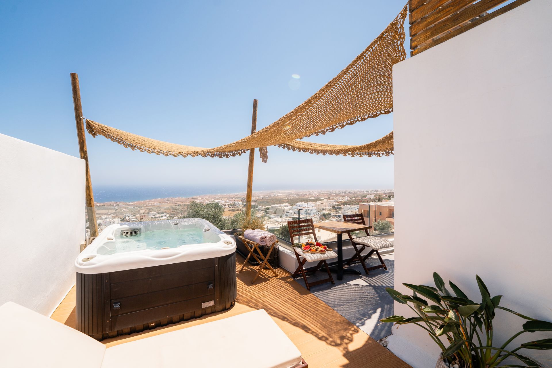 A rooftop jacuzzi with a view of the sea and dining area under a woven canopy.