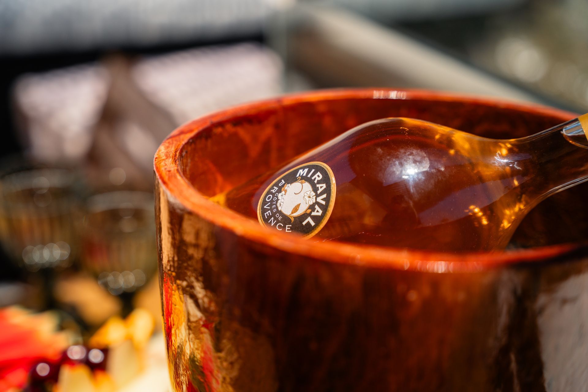 Bottle of Miravaz wine in a brown ceramic pot, resting on a platter with food.
