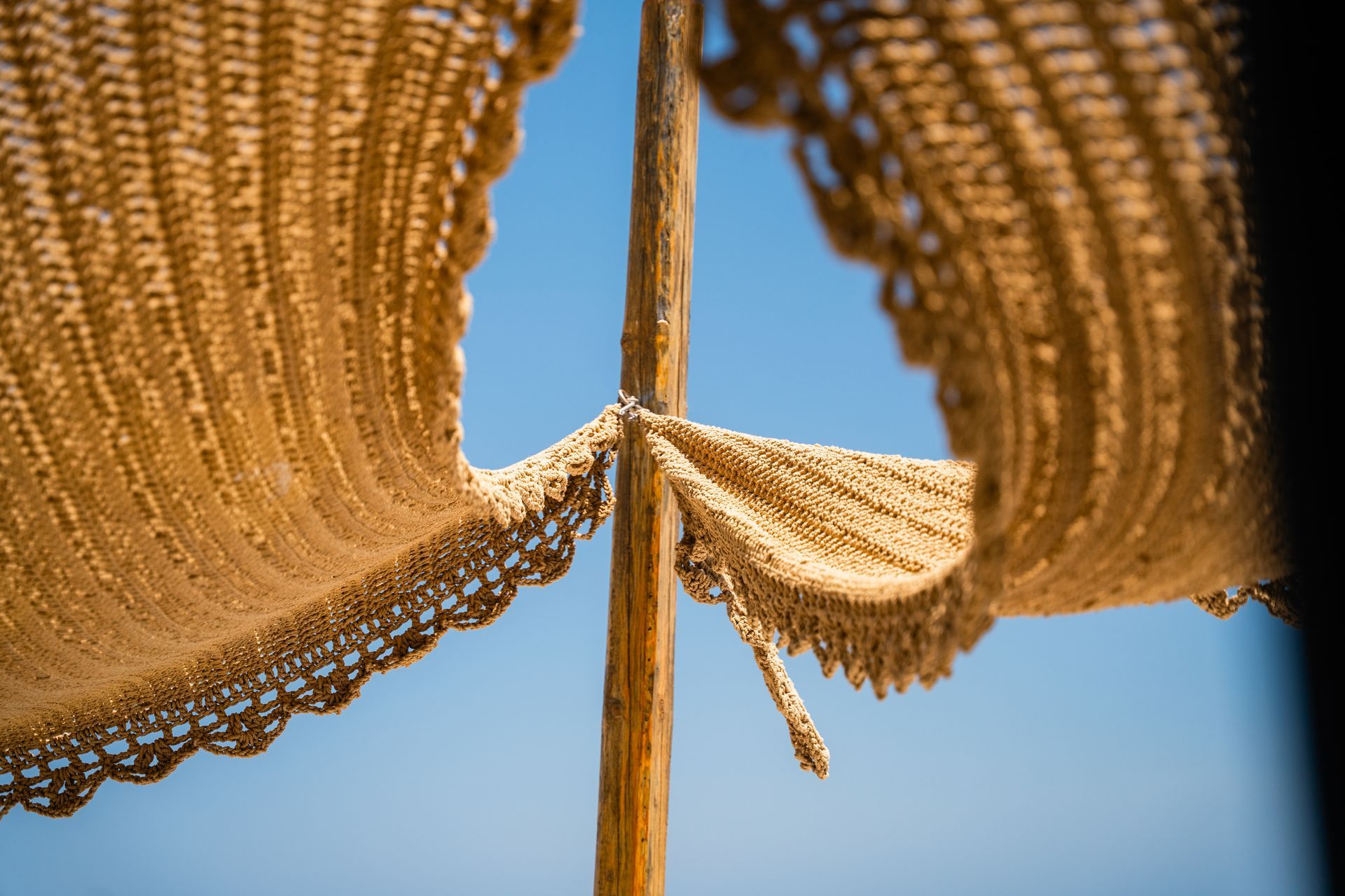 Tan woven beach umbrella against a clear blue sky.