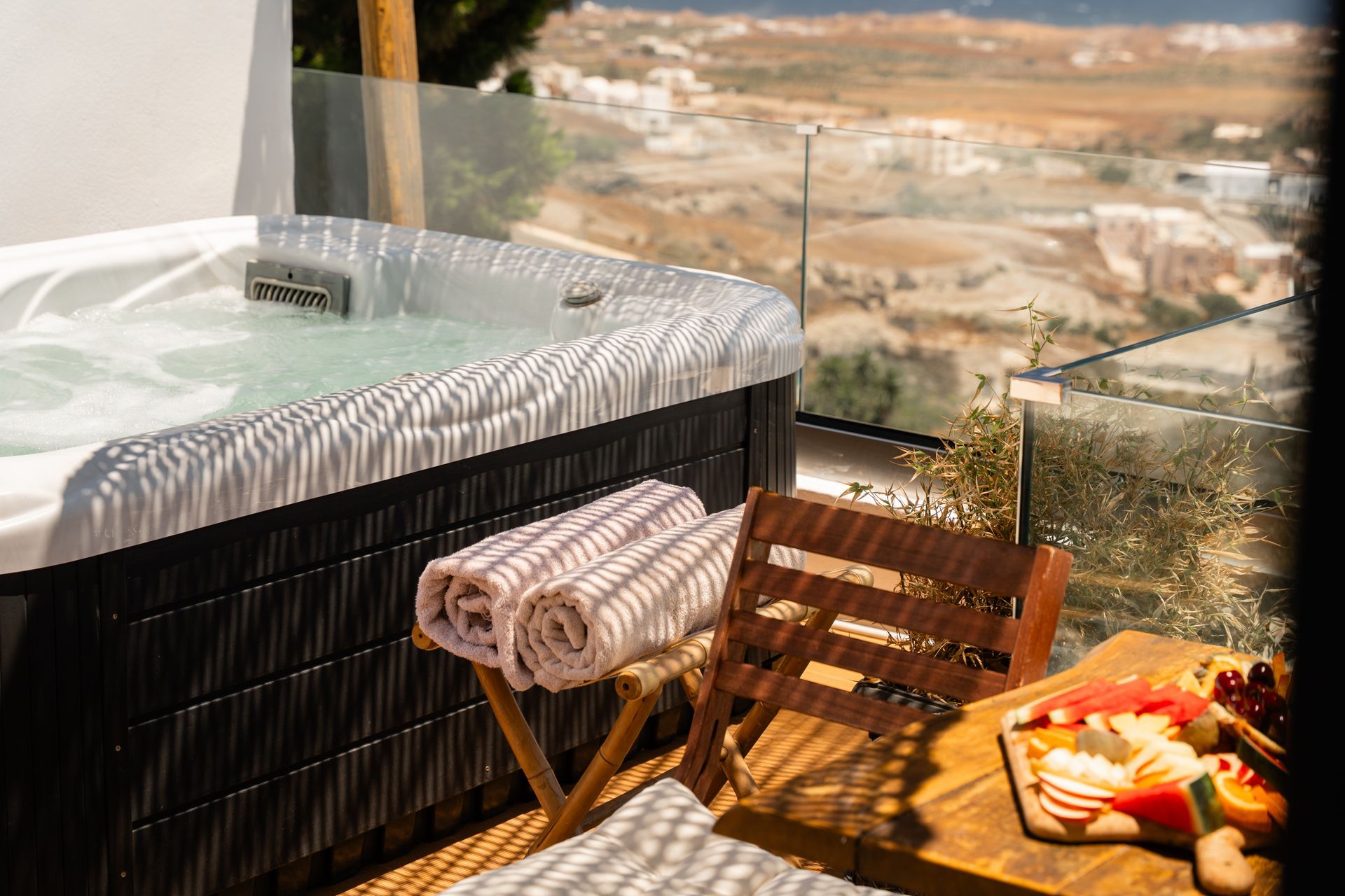 Hot tub overlooking a scenic landscape, with a small table of fruit and towels.