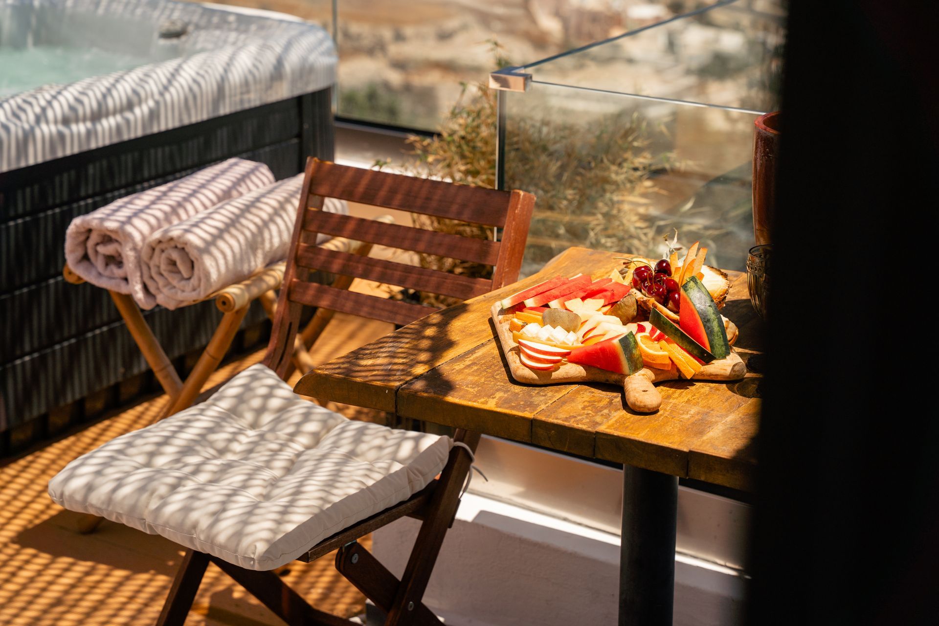 Hot tub, charcuterie board, and wooden chairs on a sunny balcony.
