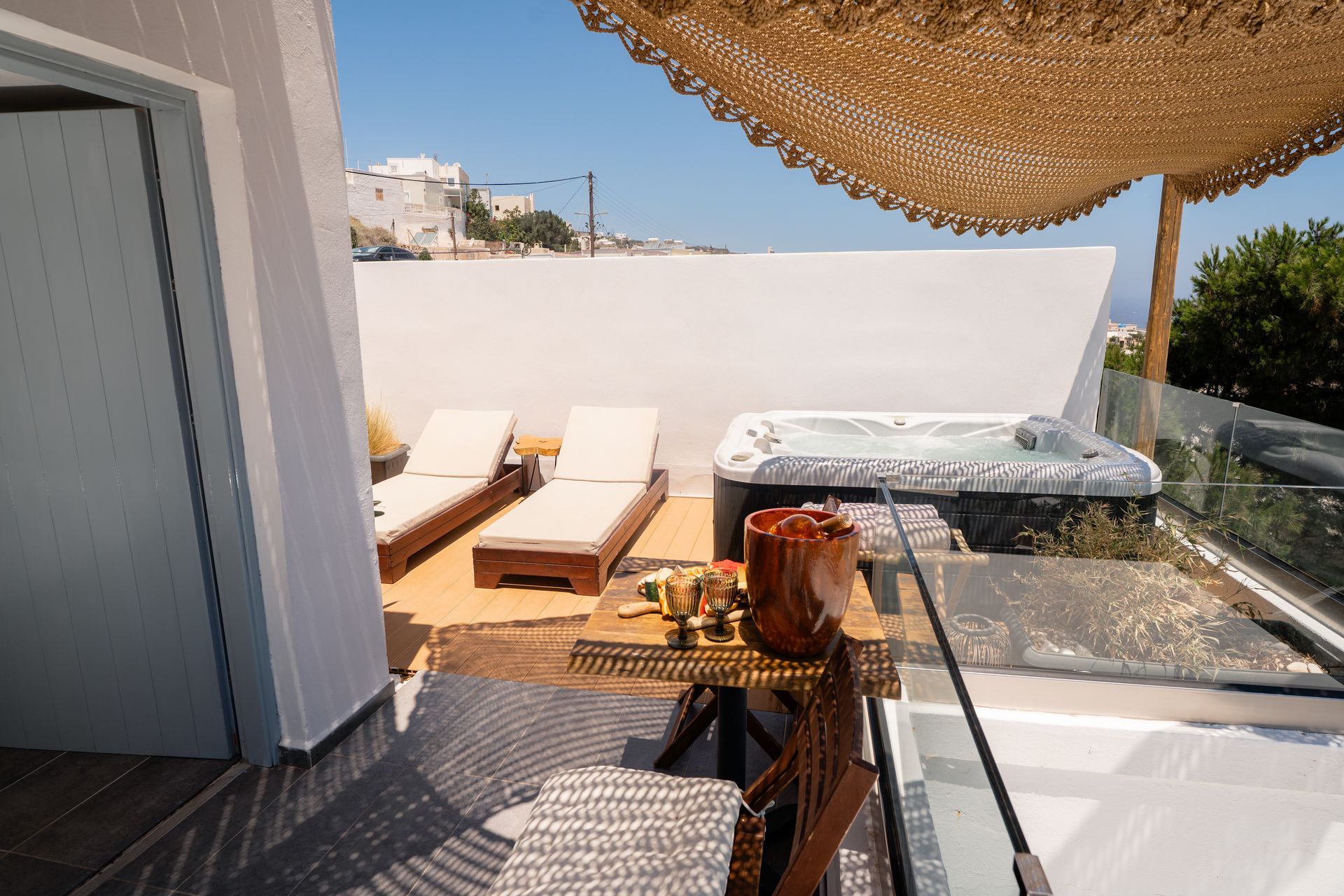 A sunny outdoor patio with a hot tub, lounge chairs, and a table set with snacks.