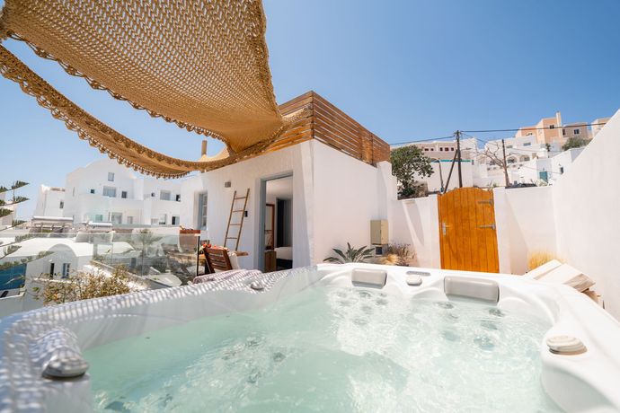Luxury rooftop hot tub with sunshade, white walls, and ocean-view terrace under a clear blue sky