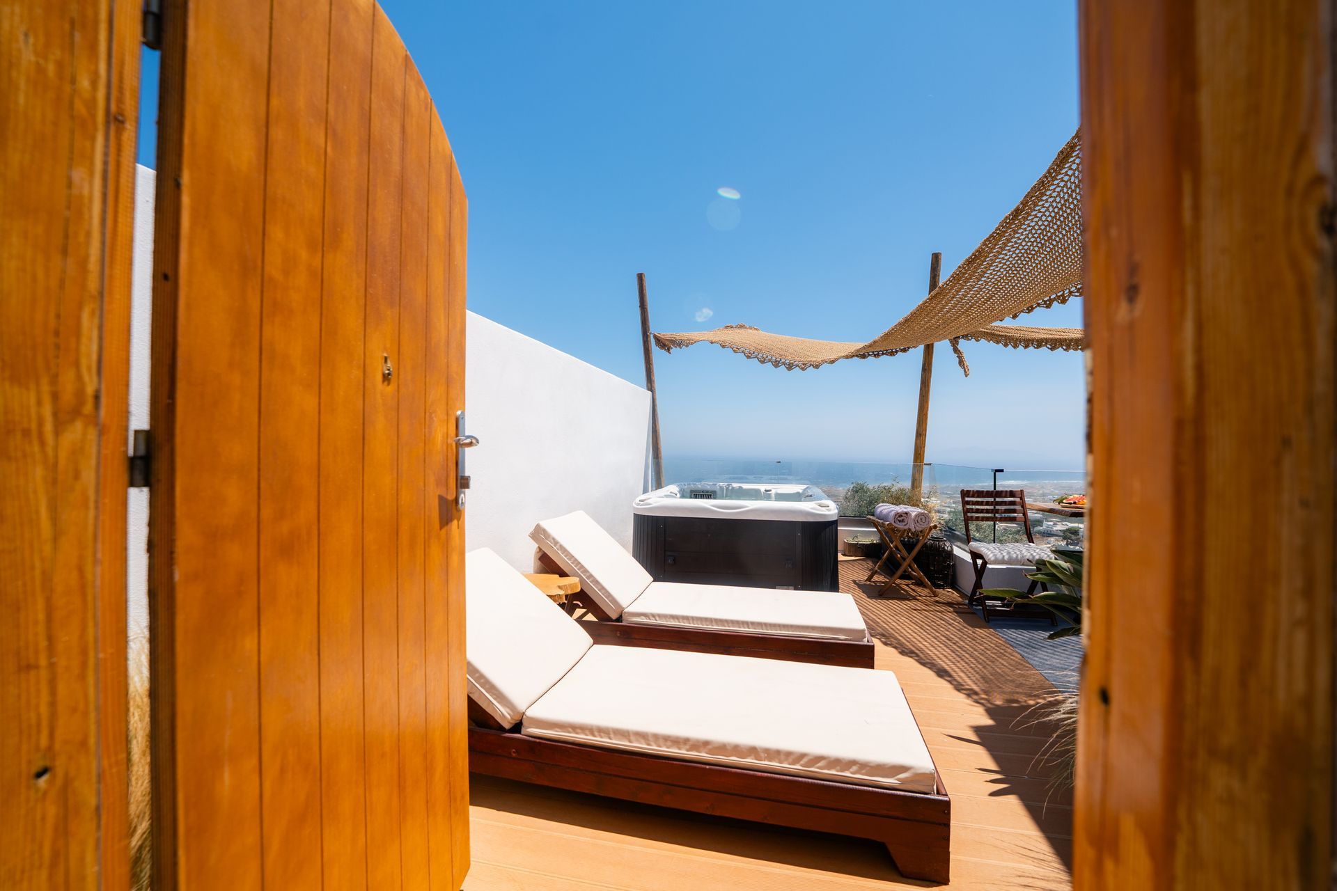 Wooden gate opens to reveal a patio with lounge chairs, a jacuzzi, and an ocean view.