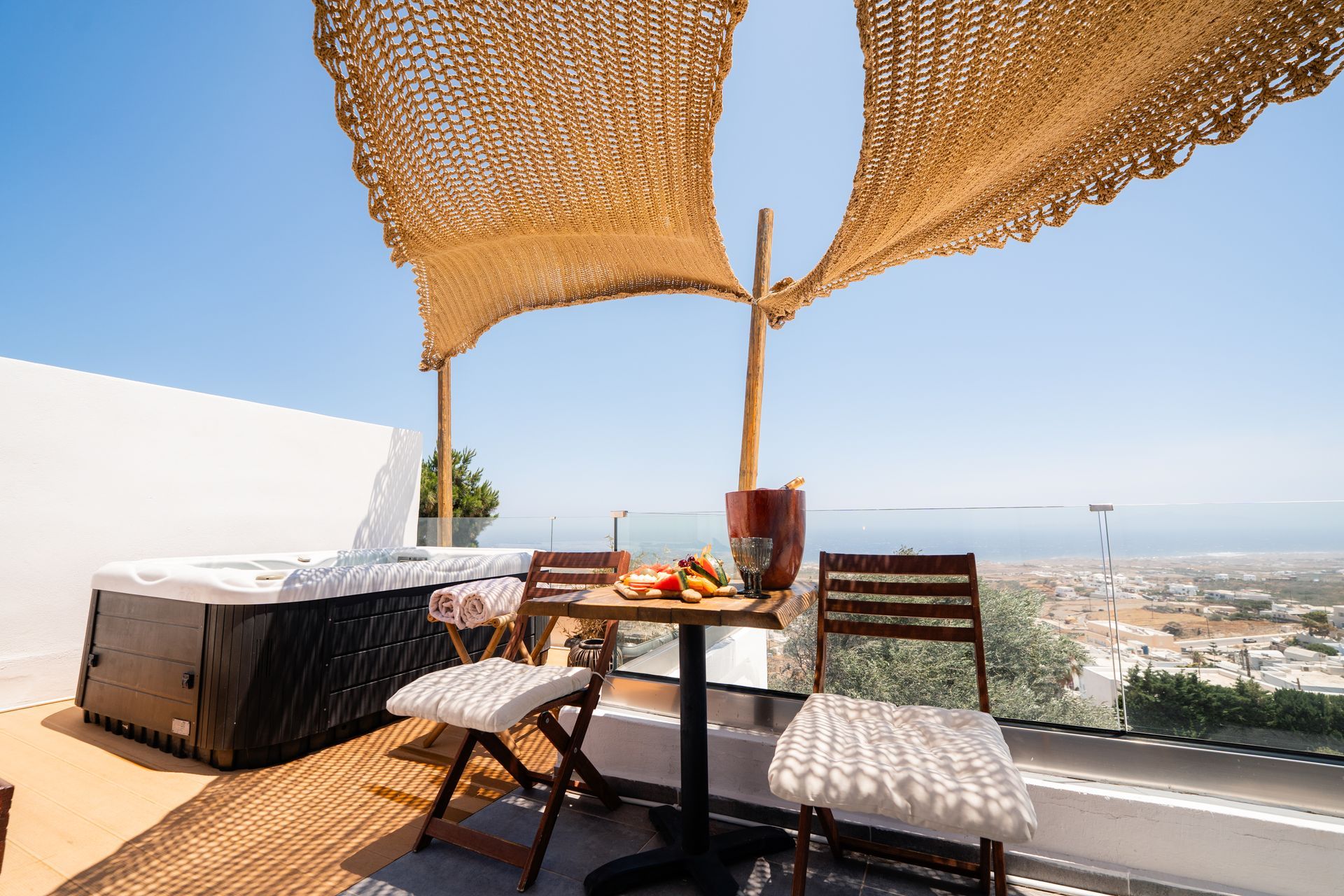 Rooftop patio with hot tub, table set for two, and city view under a sun shade.