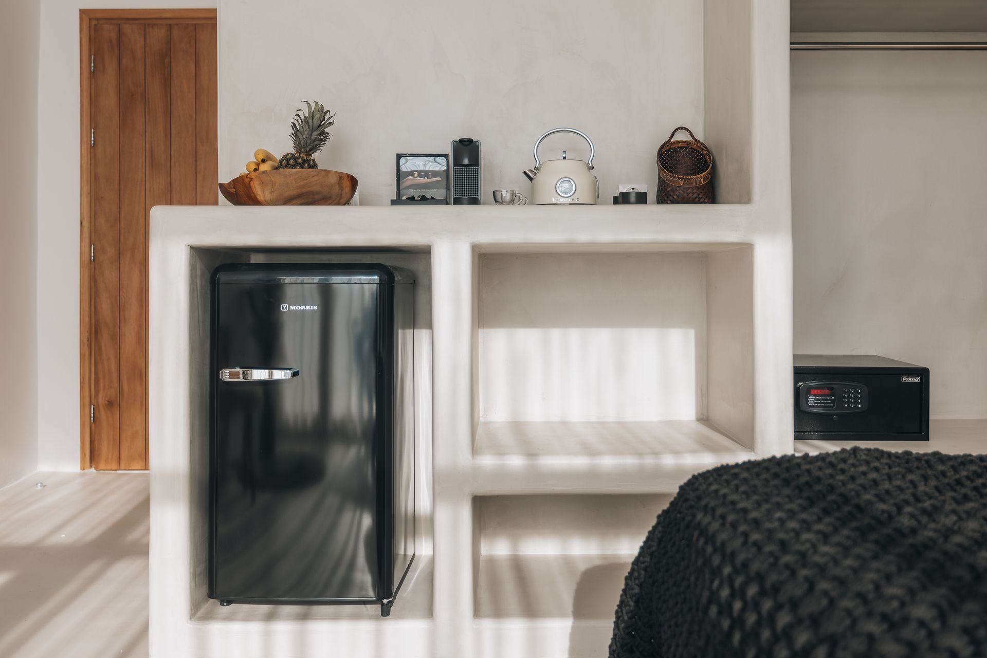 Built-in shelf with a black mini-fridge, decor, and a safe, set in a white room.