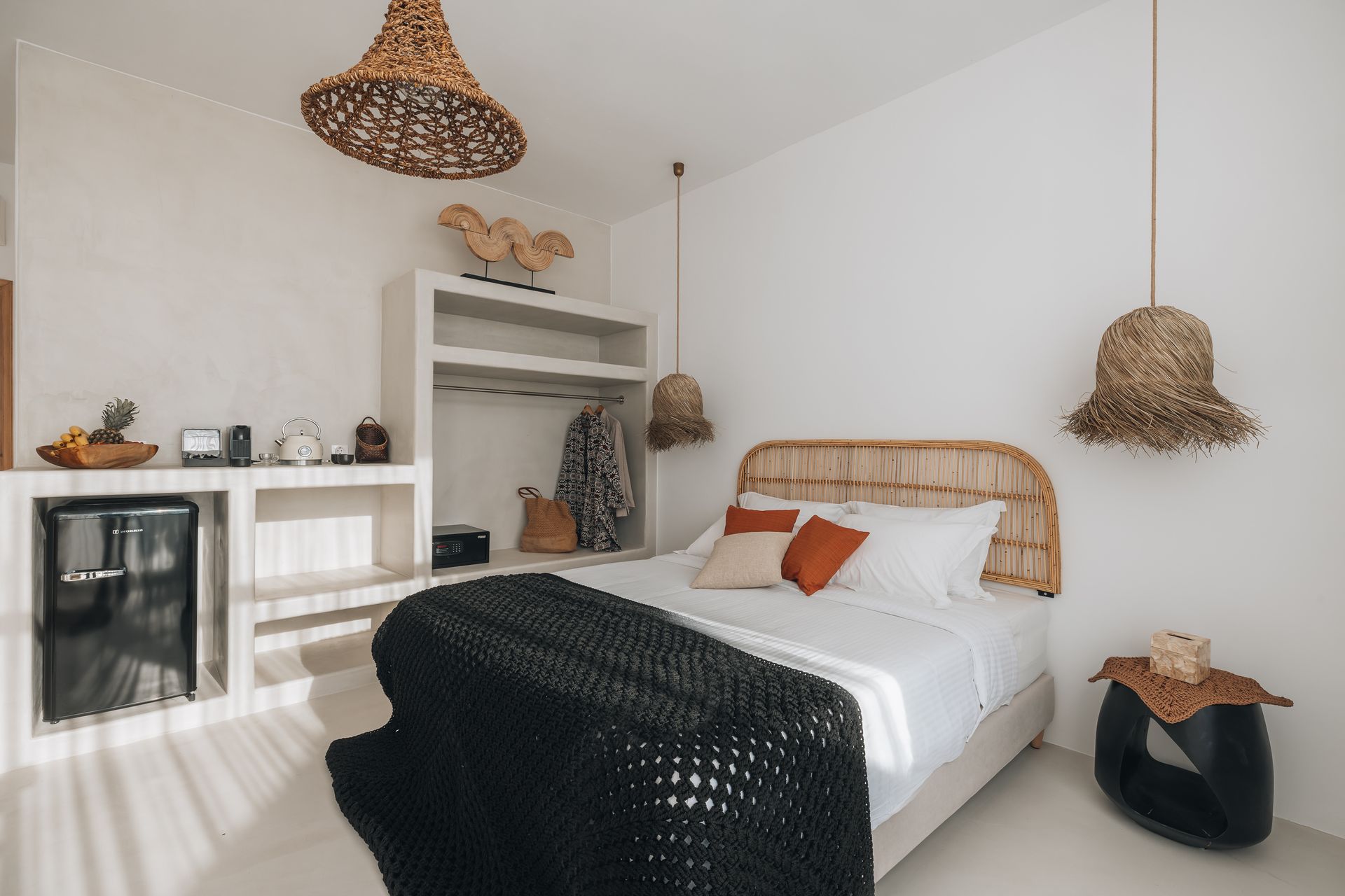 Bedroom with white walls, woven headboard, bed with orange pillows, black blanket, and woven light fixtures.