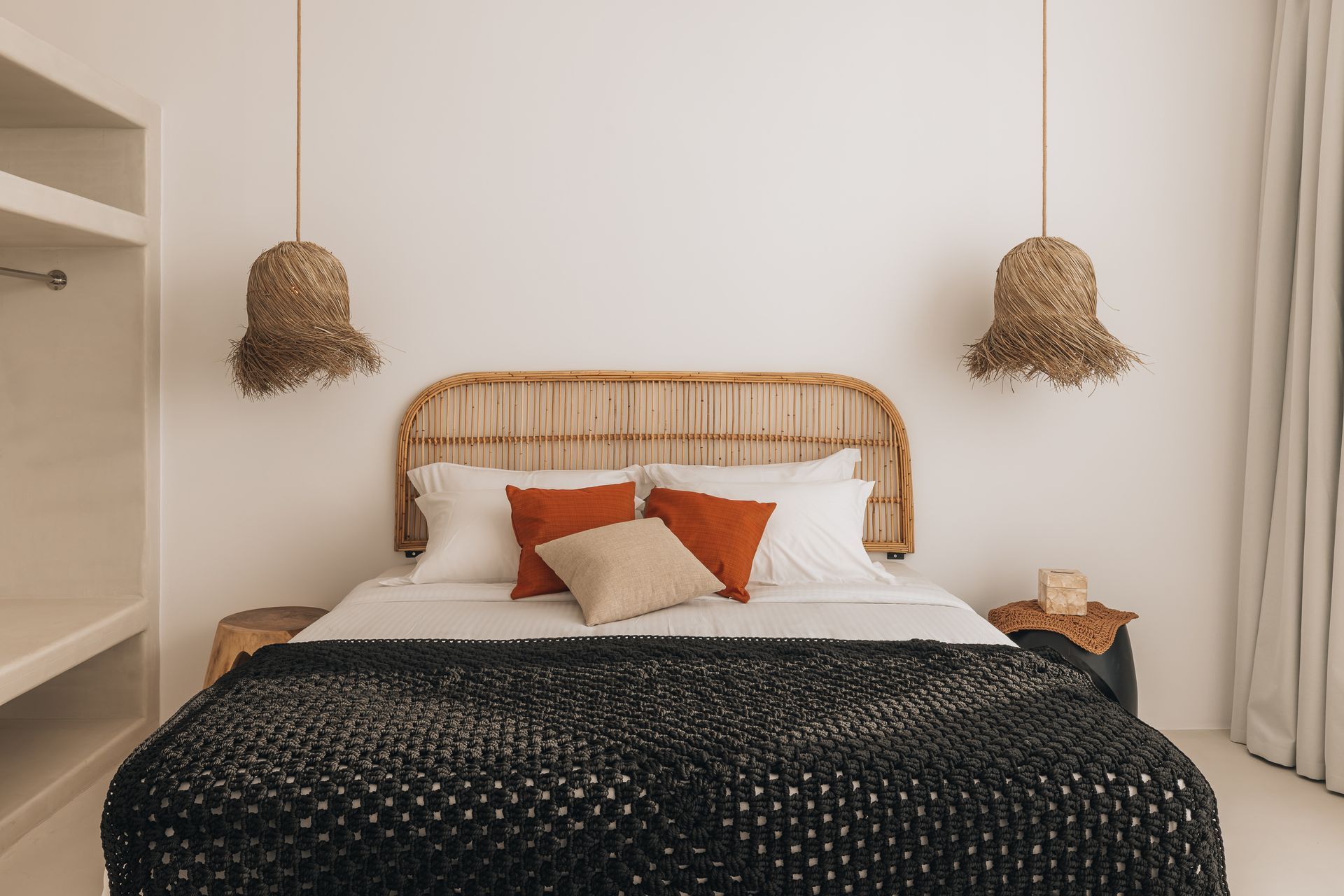 Bedroom with woven headboard, black blanket, orange and beige pillows, hanging woven lights.