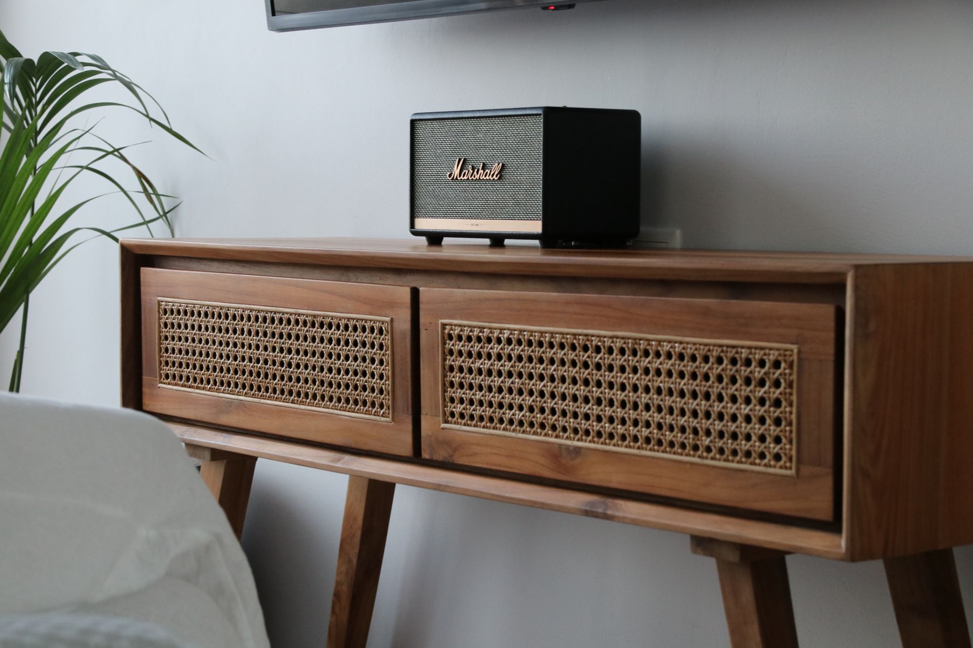 Brown wooden console with rattan doors, a Marshall speaker on top, and a plant.