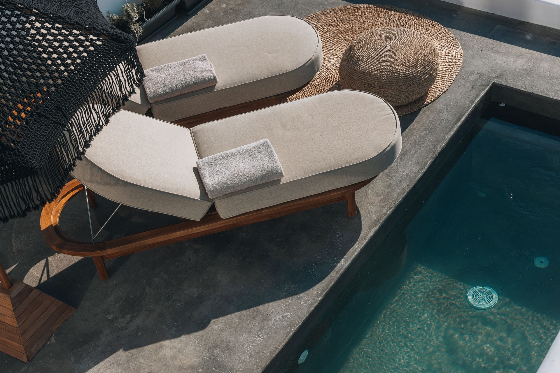 Two lounge chairs with towels beside a pool and a straw hat.