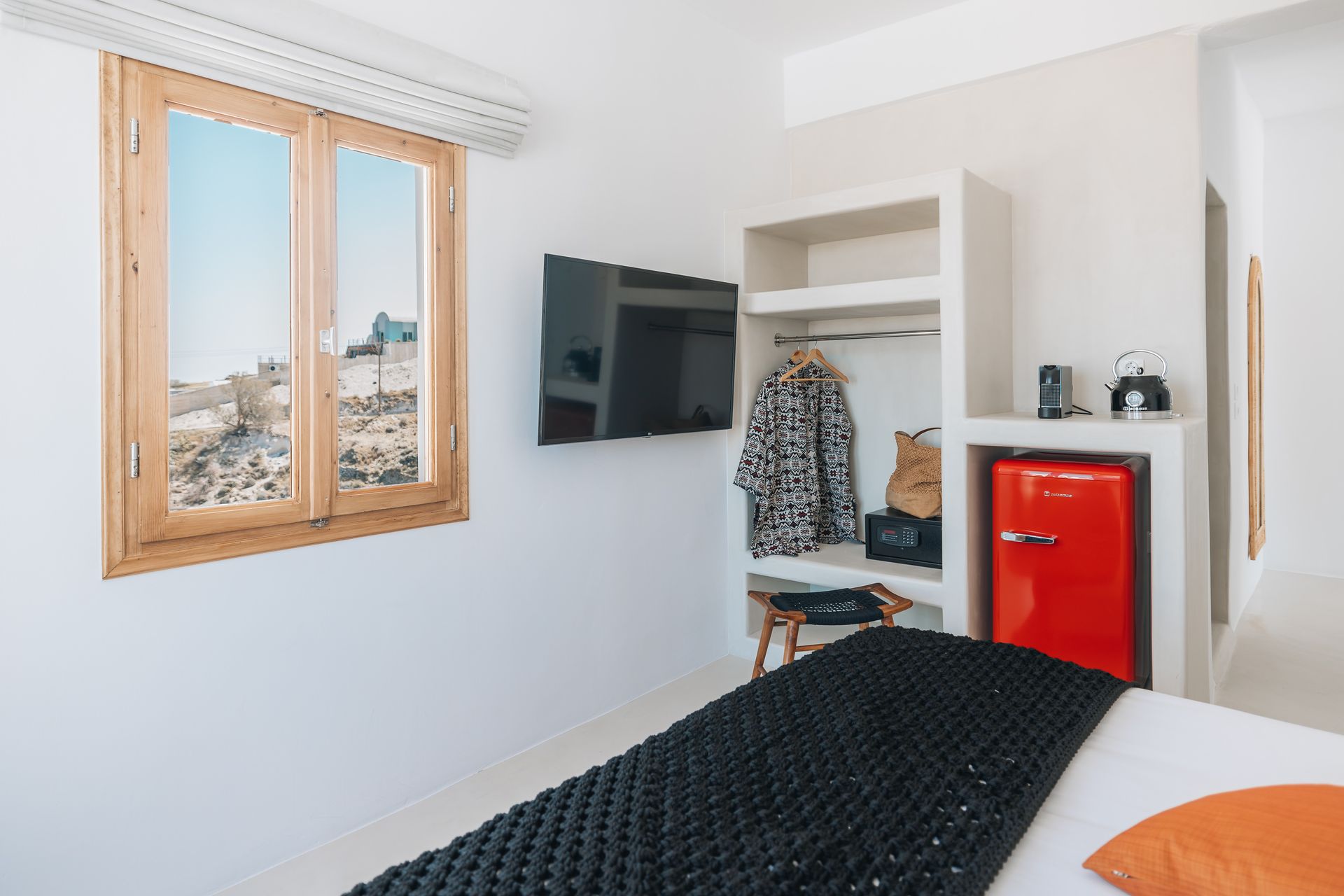 White bedroom with window, mounted TV, open closet, and a red mini-fridge.