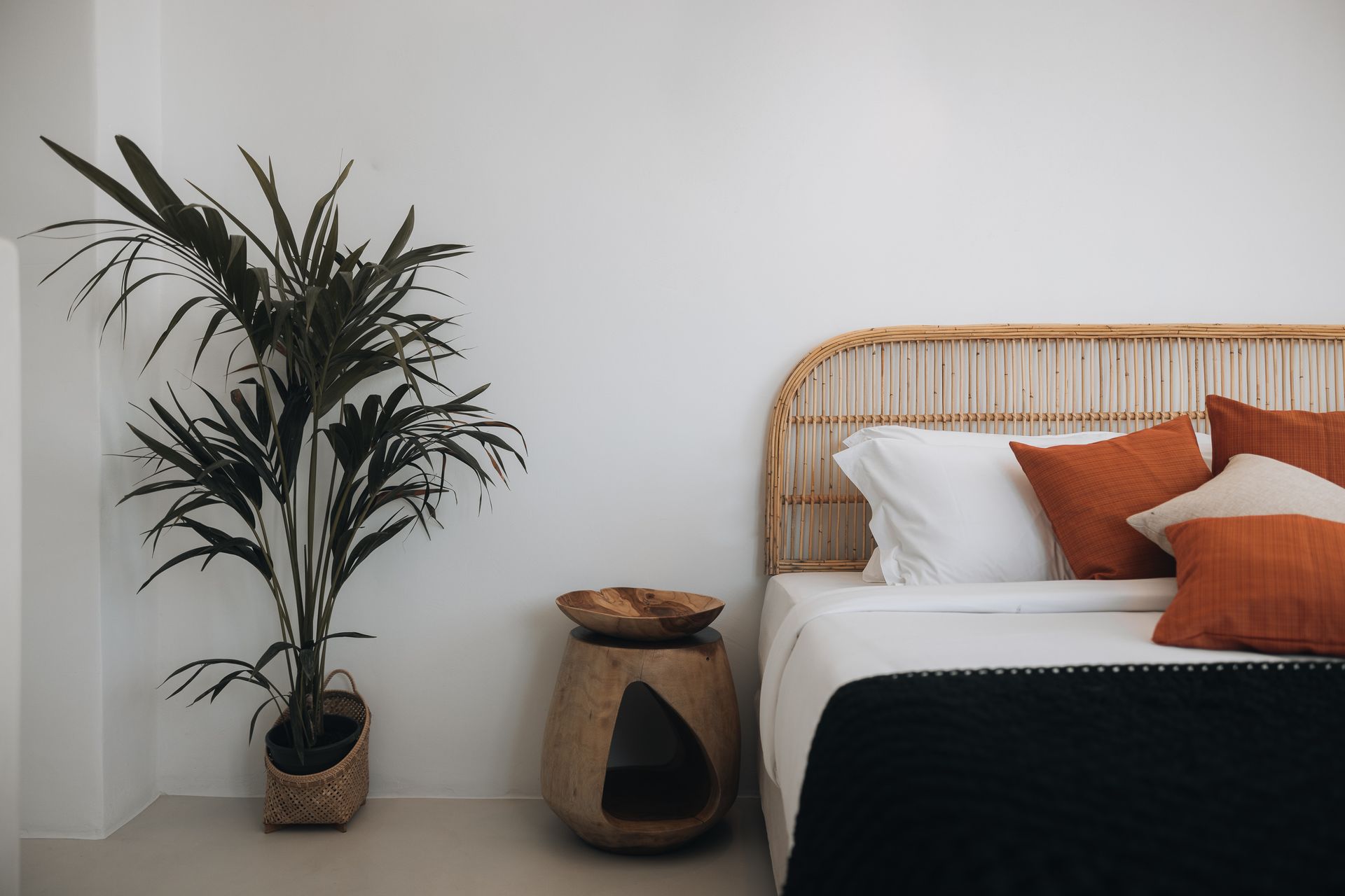 Bedroom with wicker headboard, terracotta pillows, large plant, and woven side table.