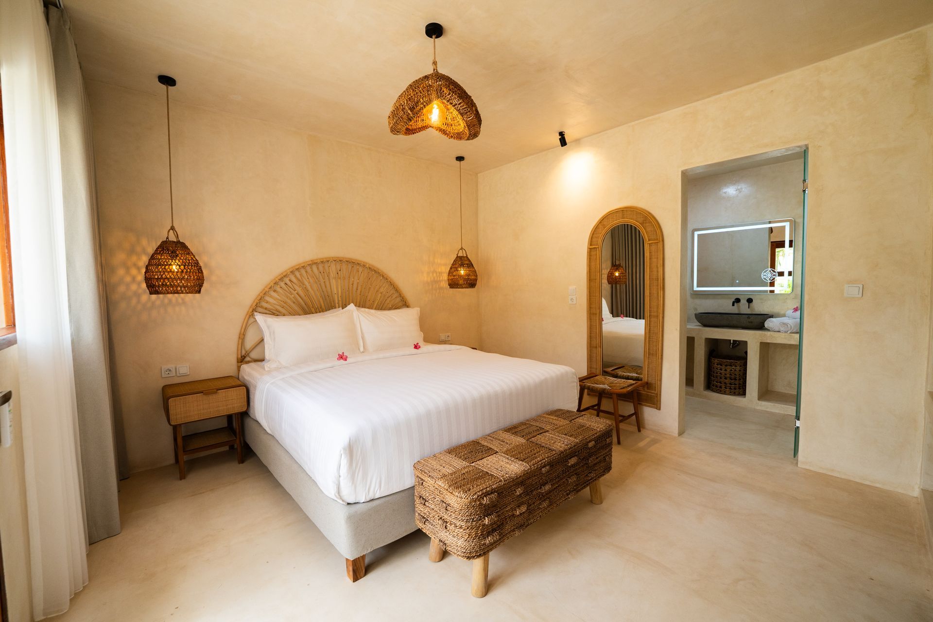 Bedroom with queen bed, rattan accents, woven lamps, and a doorway to a bathroom with a sink.