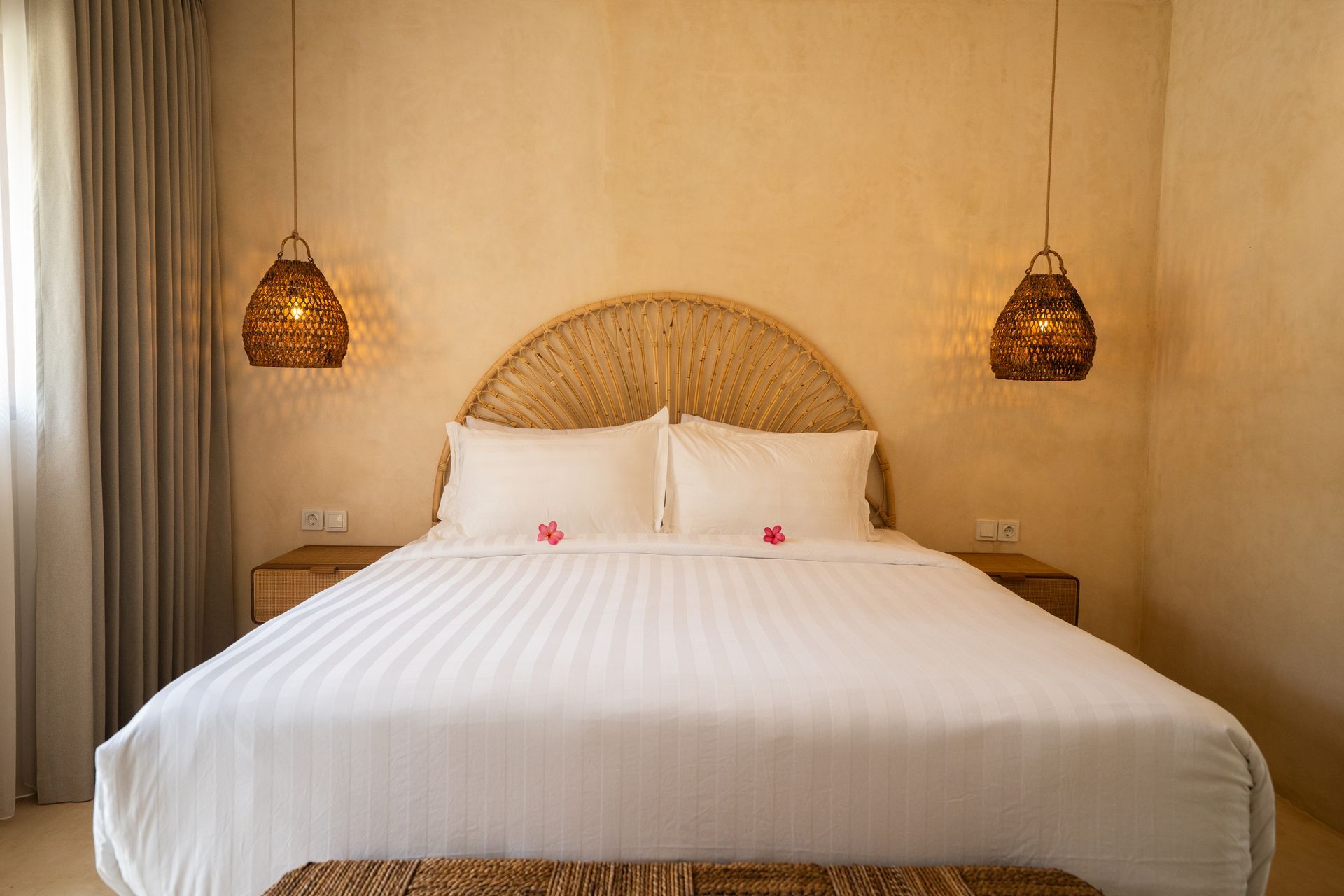 Bedroom with a king-sized bed, woven headboard, pendant lights, and cream-colored walls.
