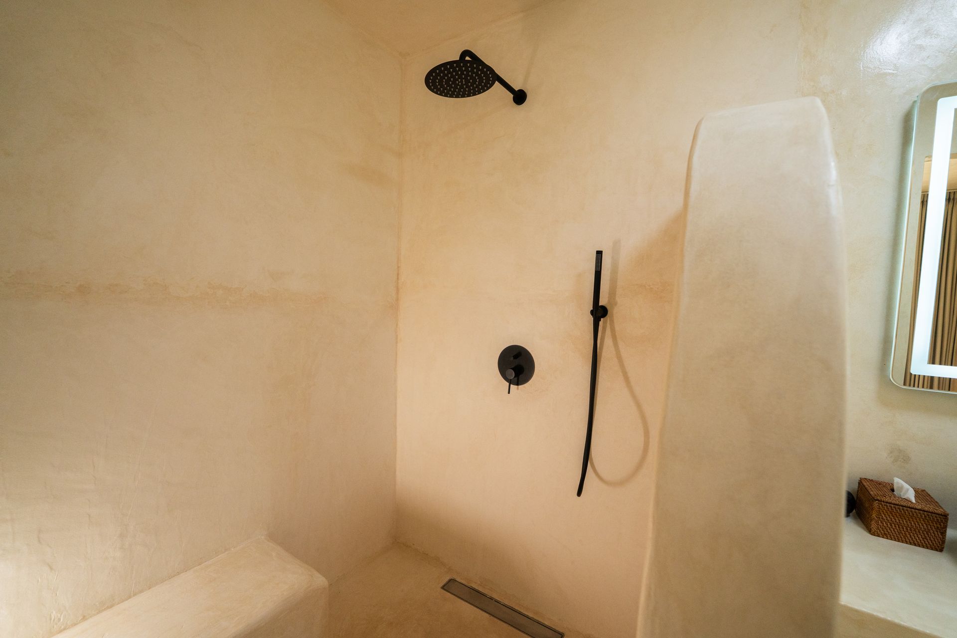 Shower with beige walls, black showerheads, and a built-in bench.