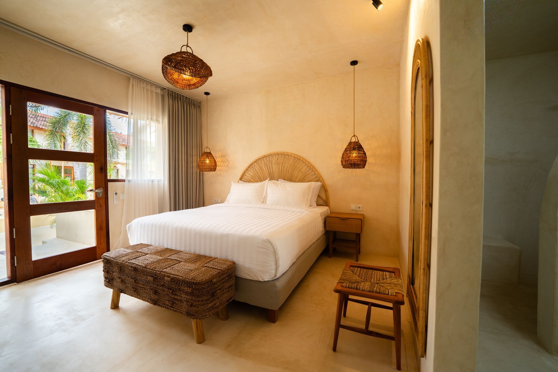 Bedroom with neutral tones, wicker headboard, pendant lights, and a wooden bench.