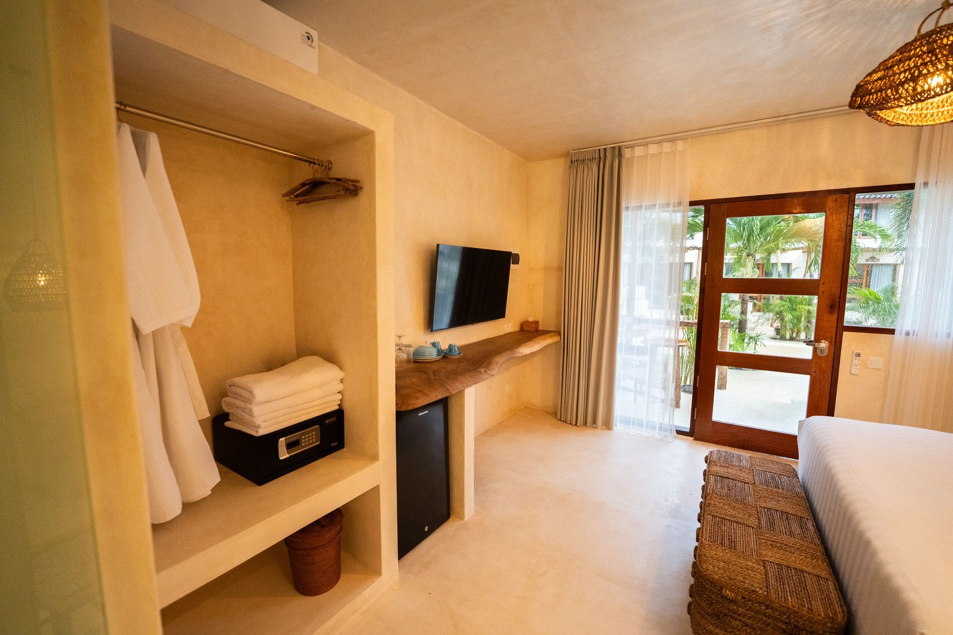 Bedroom with closet, TV, and open door to balcony. Tan walls, white bedding, wooden accents.