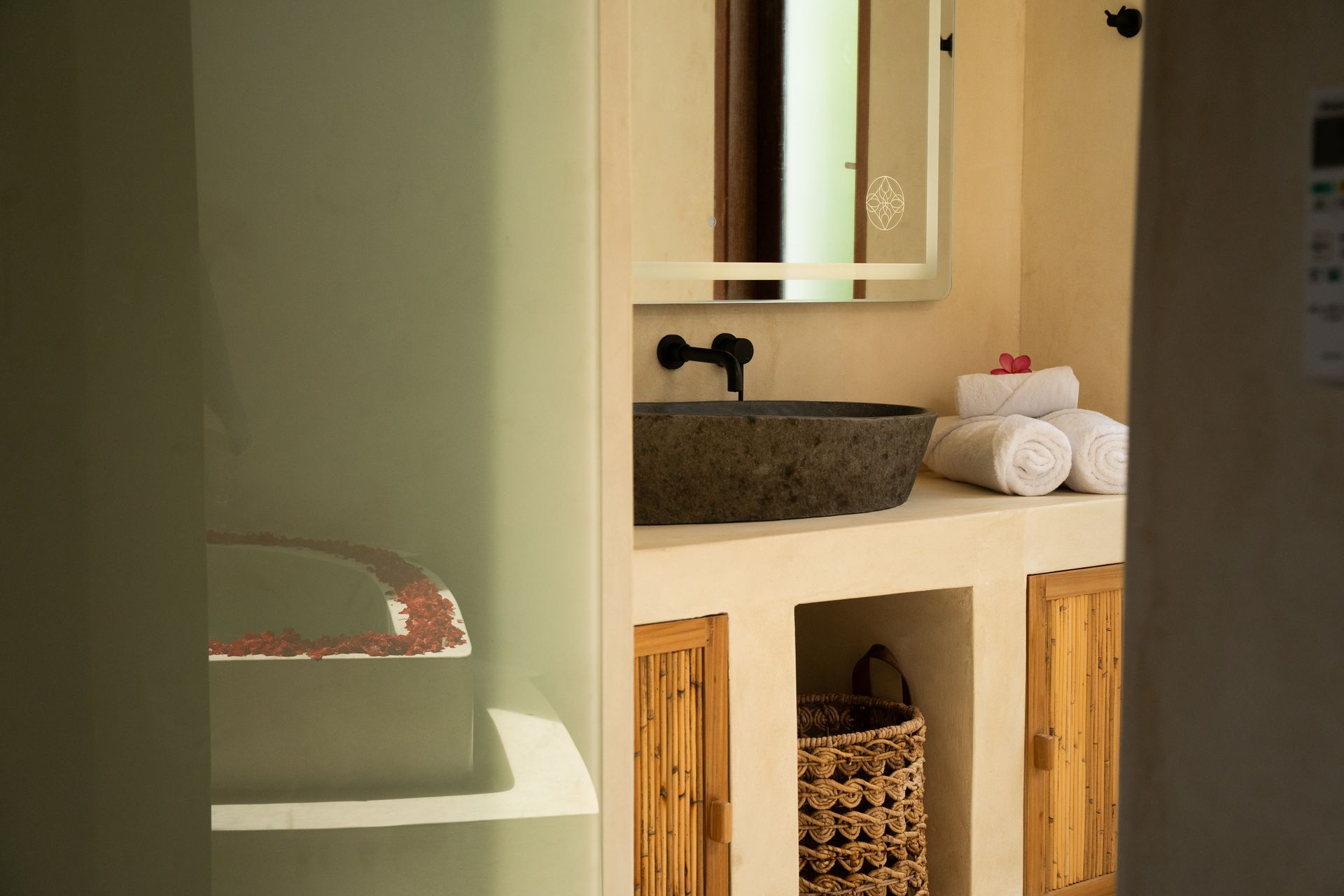 Bathroom with stone sink, white walls, and wooden cabinet. Towels and a basket are visible.