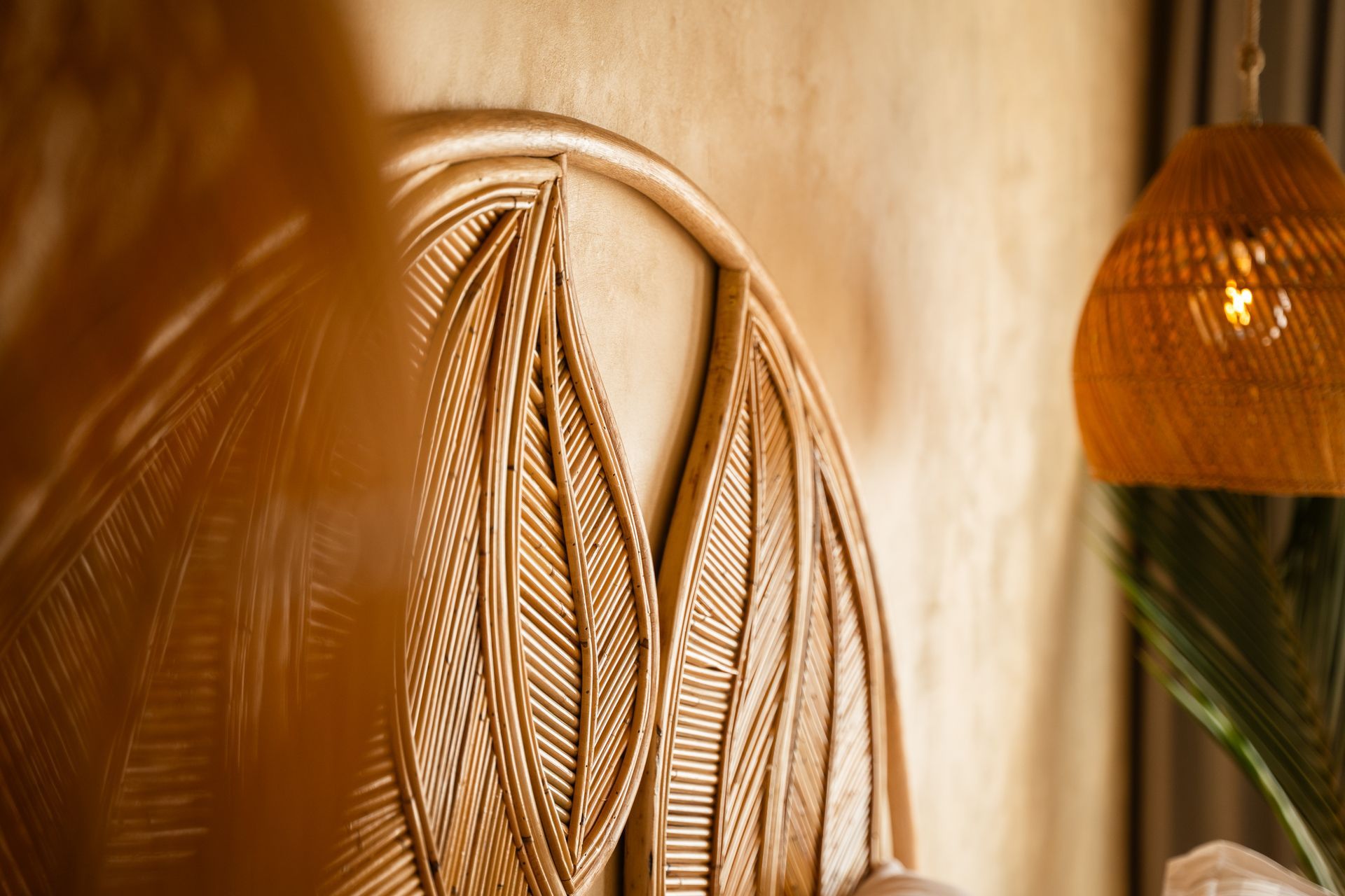 Woven wooden headboard with leaf design, next to a rattan lamp and palm fronds.