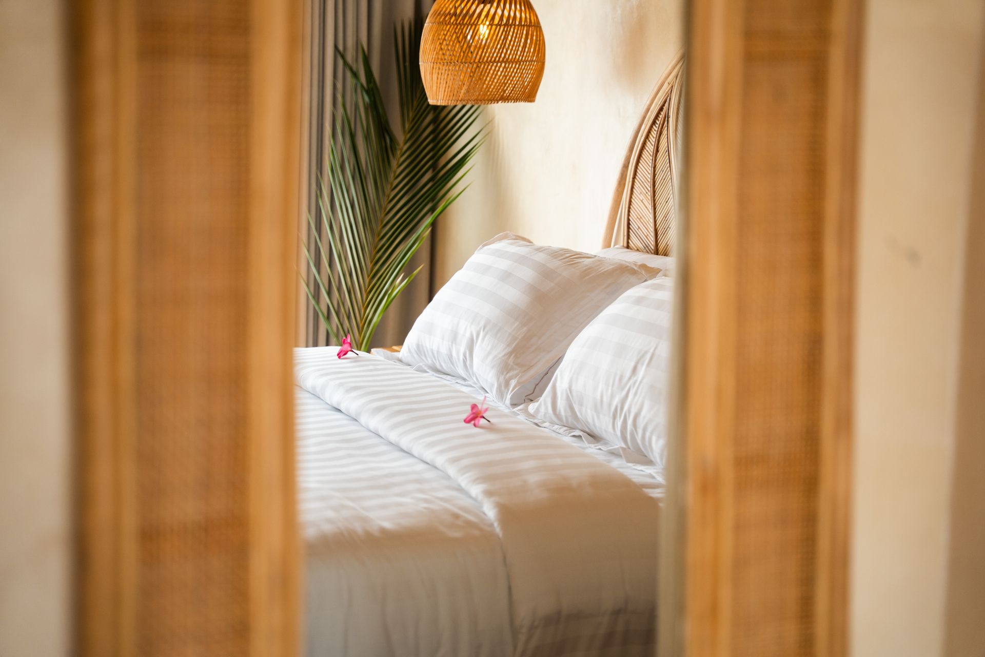A bed with white linens reflected in a wooden framed mirror, a natural, relaxing setting.