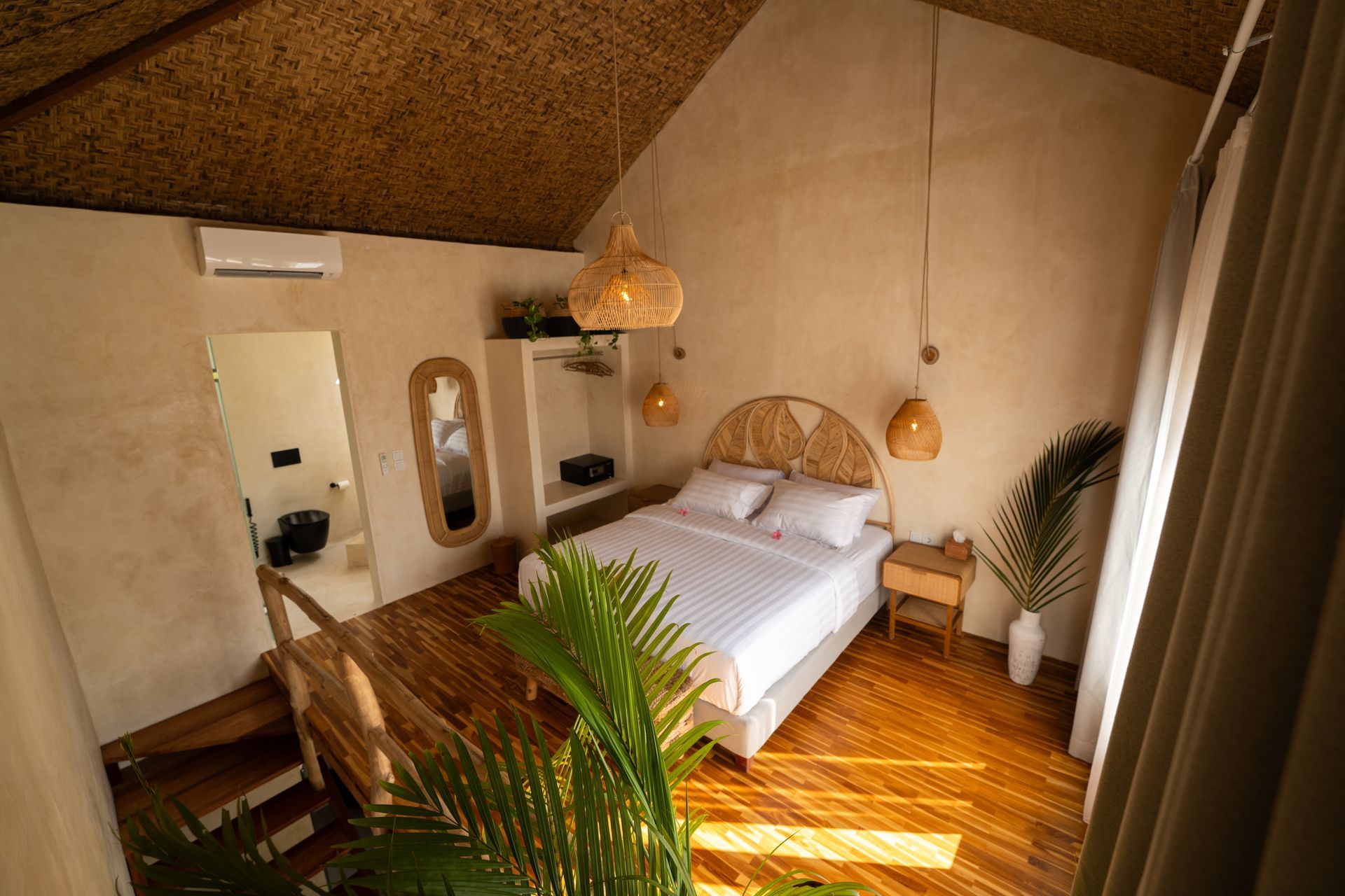 Bedroom with bamboo flooring, a bed, and a bathroom viewed from above. Natural light and neutral tones.